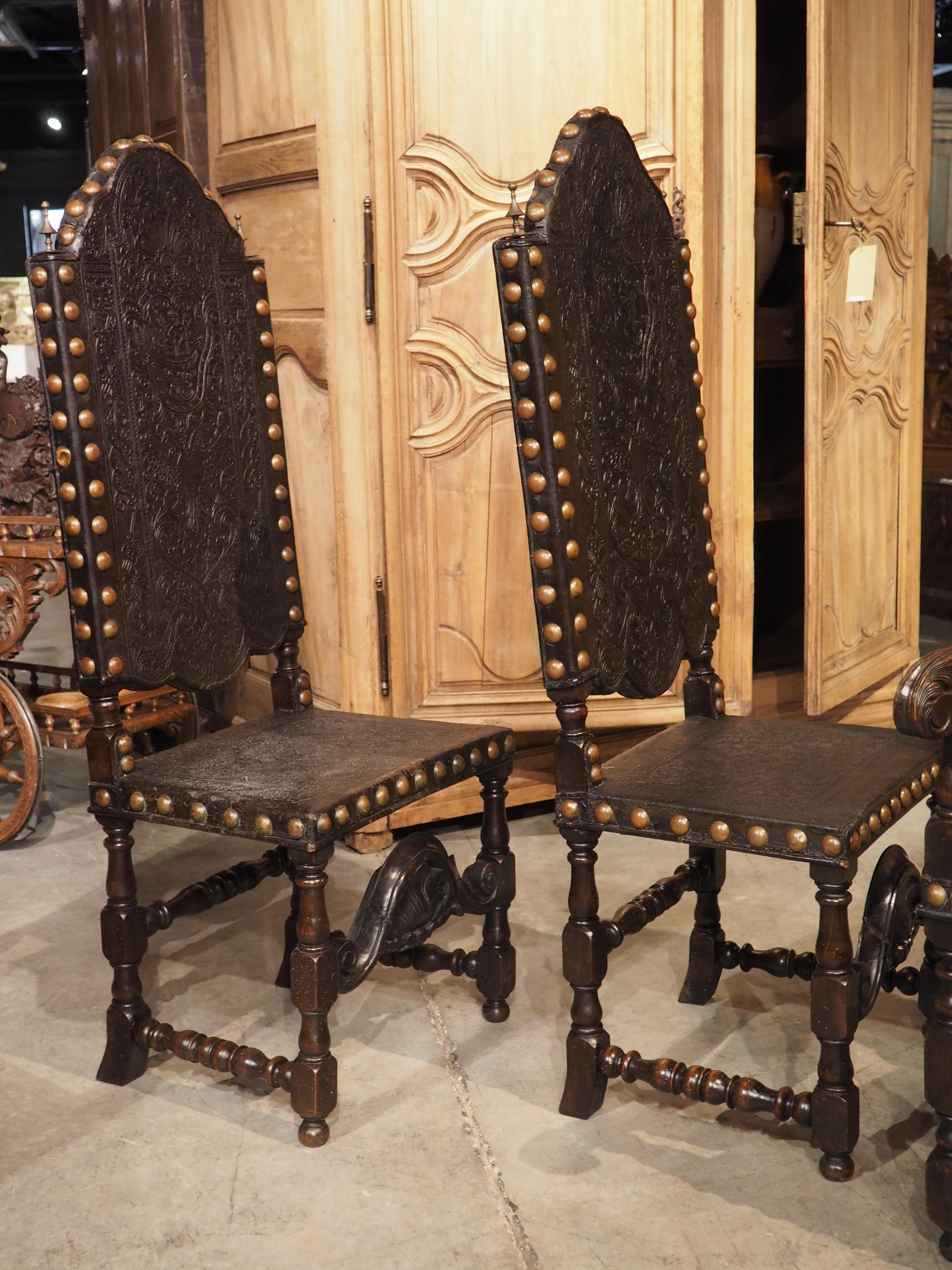 An exquisite set of eight Spanish chairs, featuring a harmonious blend of artistry and craftsmanship. This elegant collection is comprised of four armchairs and four side chairs, each meticulously adorned with embossed leather affixed by numerous