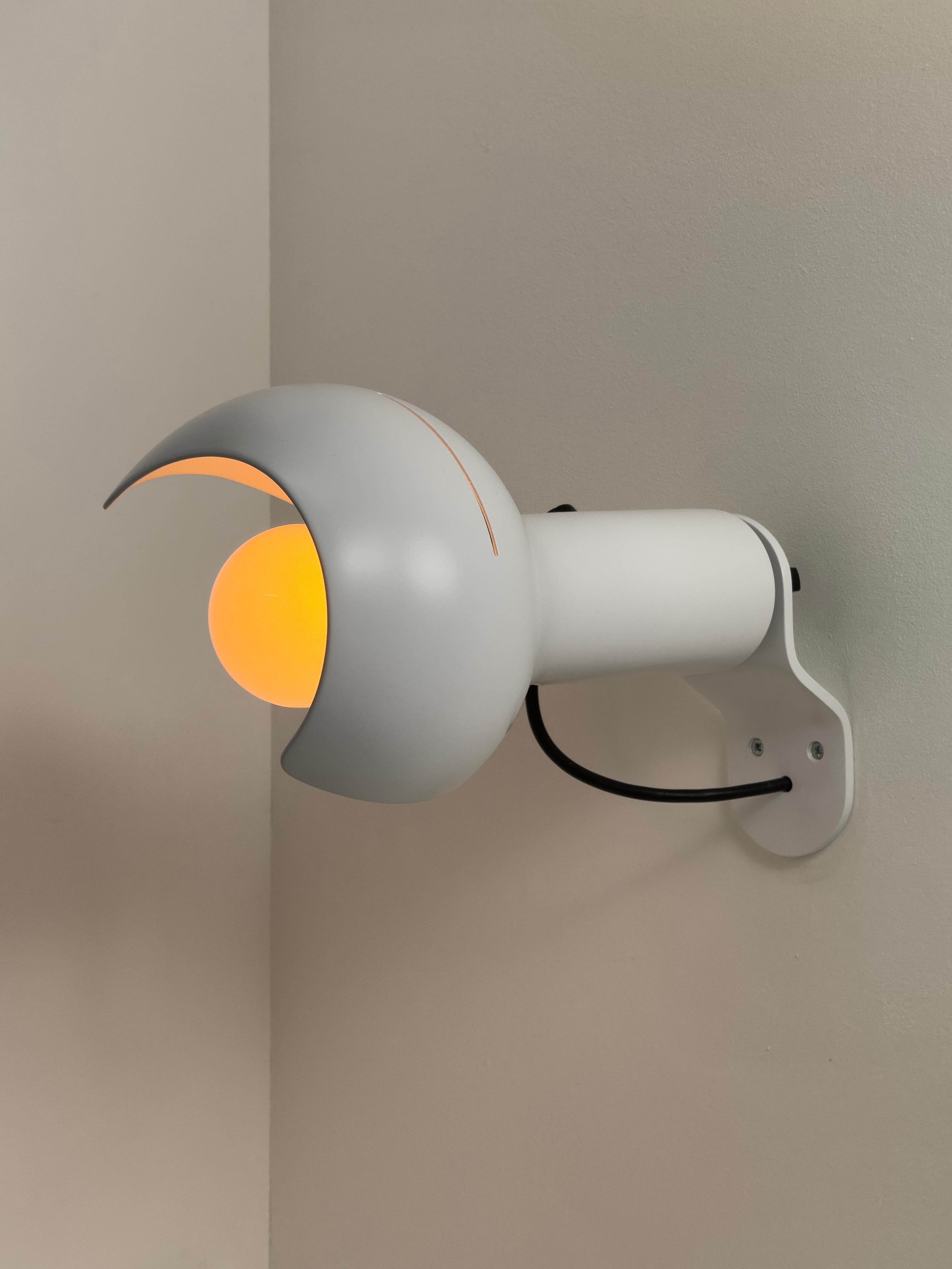 Ogni lampada è dotata di un paralume in alluminio a forma di calice e rifinito in lacca bianca opaca. Una manopola in plastica nera permette di regolare l'angolo di rotazione del corpo principale. Progettato e prodotto in Italia negli anni