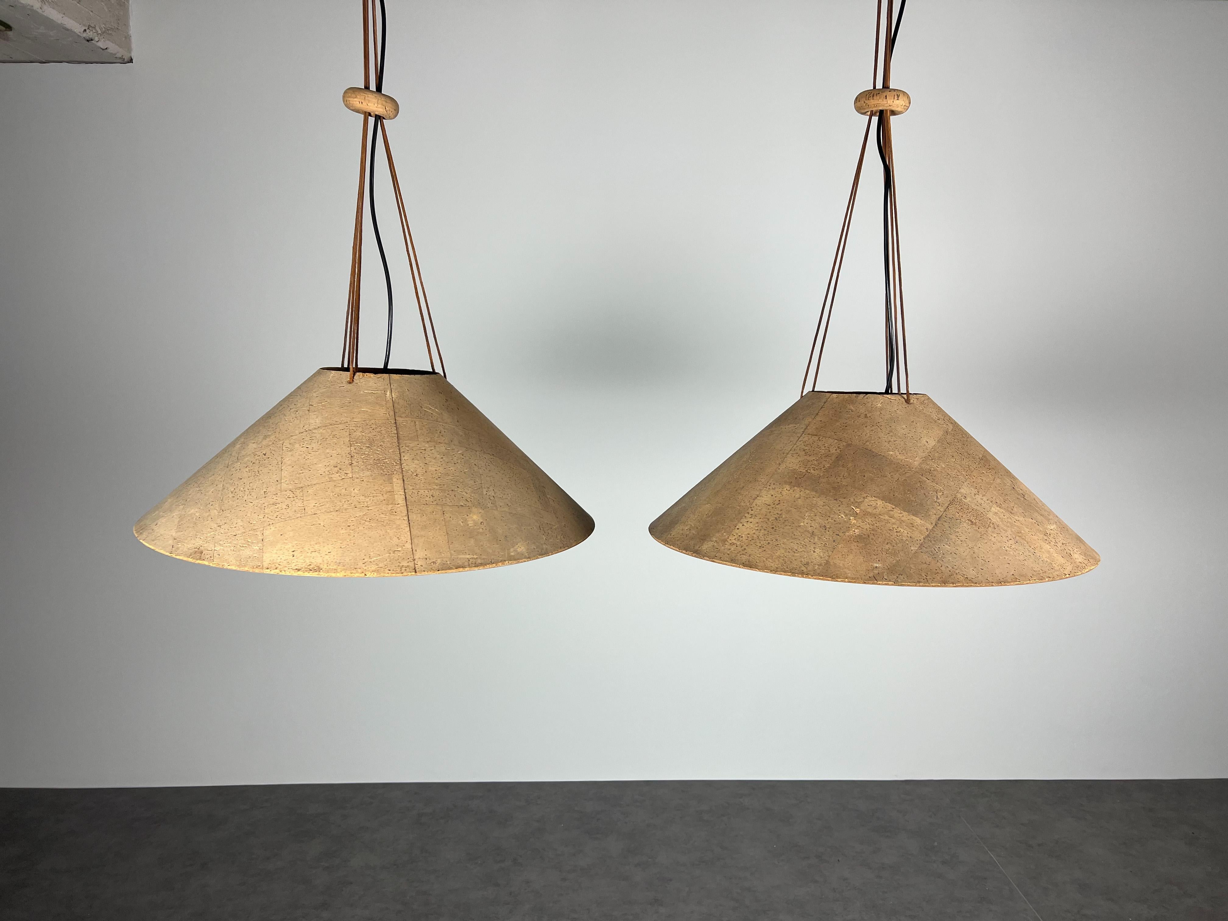 Unique worldwide set of two very rare Cork pendant lamps by Wilhelm Zannoth for M Design (Ingo Maurer).
Both Pendants are in original condition with light-brown laquered metal inner shade. The hight of the Lamps can be adjusted via the leather