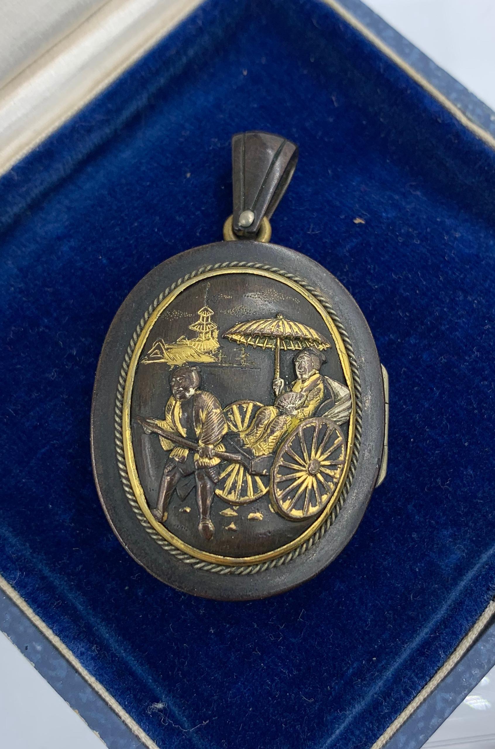 Here we have a very rare Japanese Shakudo Locket Pendant with images of a bird or quail in a forest with Mount Fuji in the background on one side and a woman riding in a rickshaw passing a temple on the other side.  The locket is a stunning example