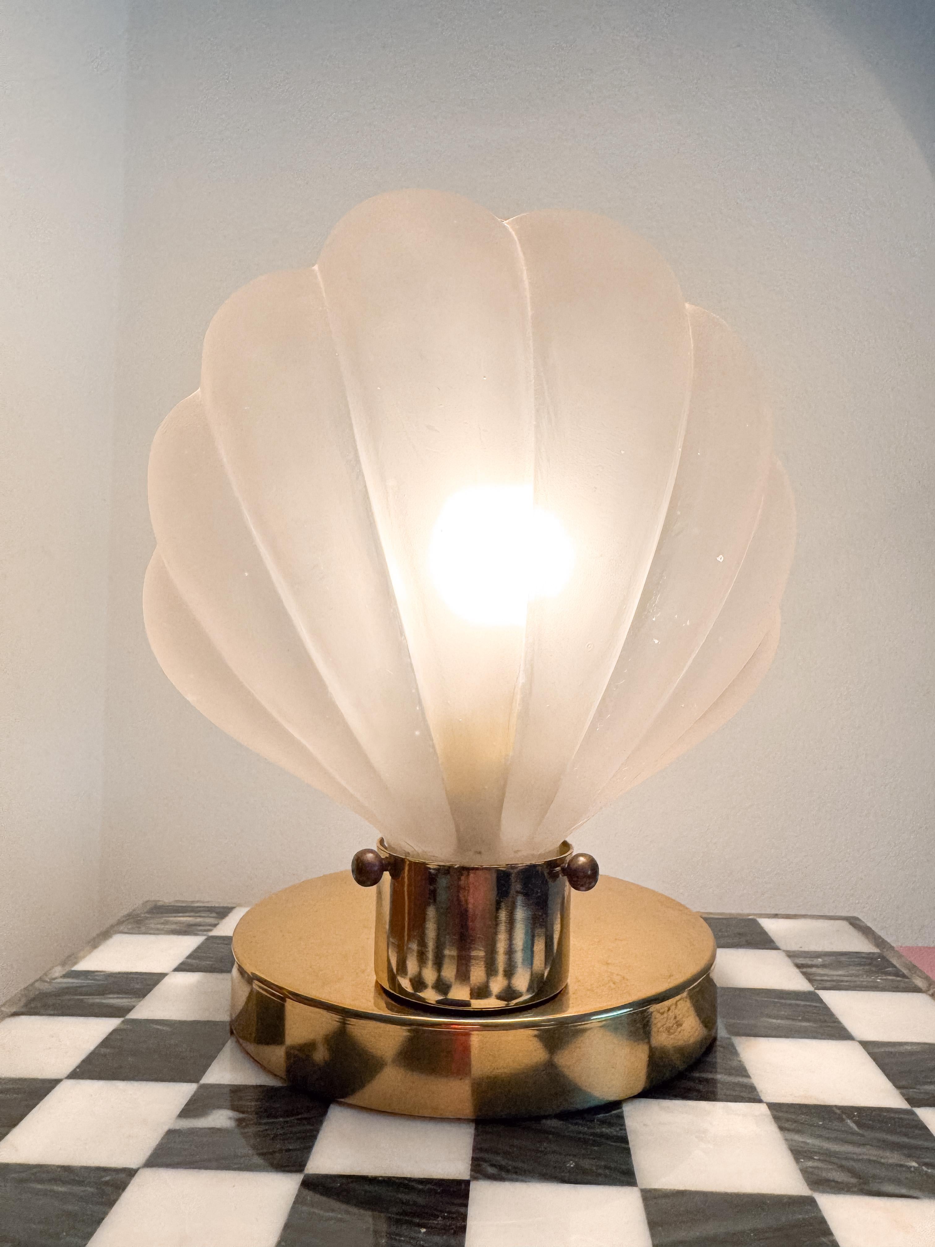 Striking and sculptural, this rare 1980s table lamp captures the essence of Art Deco elegance with a bold twist from the glam-infused '80s. The shell-shaped frosted glass body is framed in polished brass, giving it a refined yet statement-making