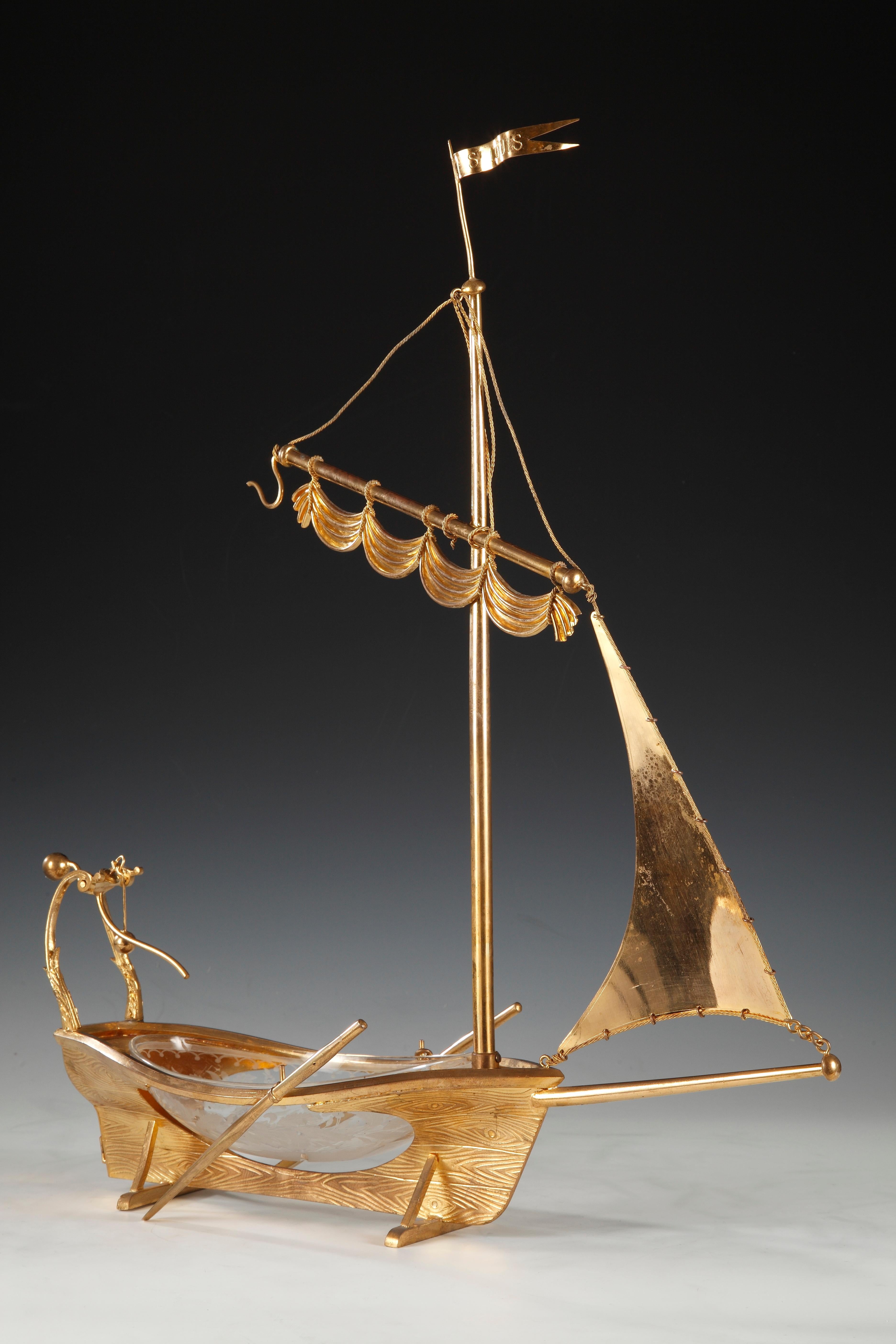 Boat-like center table made of crystal and gilt bronze, whose chasing imitates wood grain on the hull, attributed to the Cristallerie Saint-Louis. Equipped with its oars, its mobile rudder, its ropes and with a mast on which the flag “Le St-Louis”.