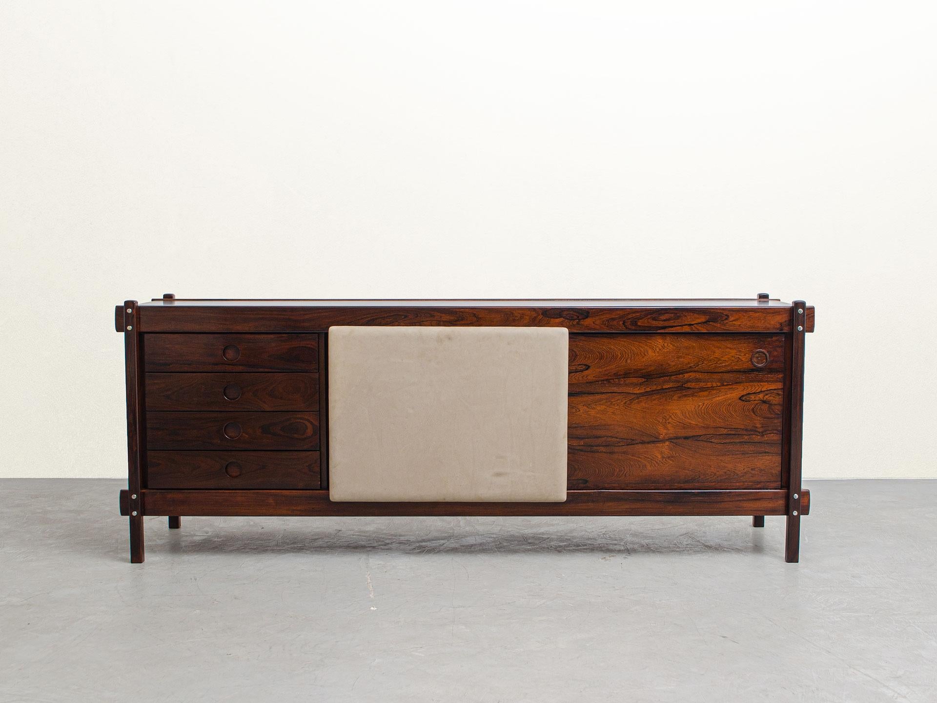 This beautiful sideboard was conceived in the 60s by Sérgio Rodrigues.

The piece is made of solid Brazilian hardwood. One of the doors is nicely covered in suede and the other door is in veneer. There are four deep and very useful drawers for