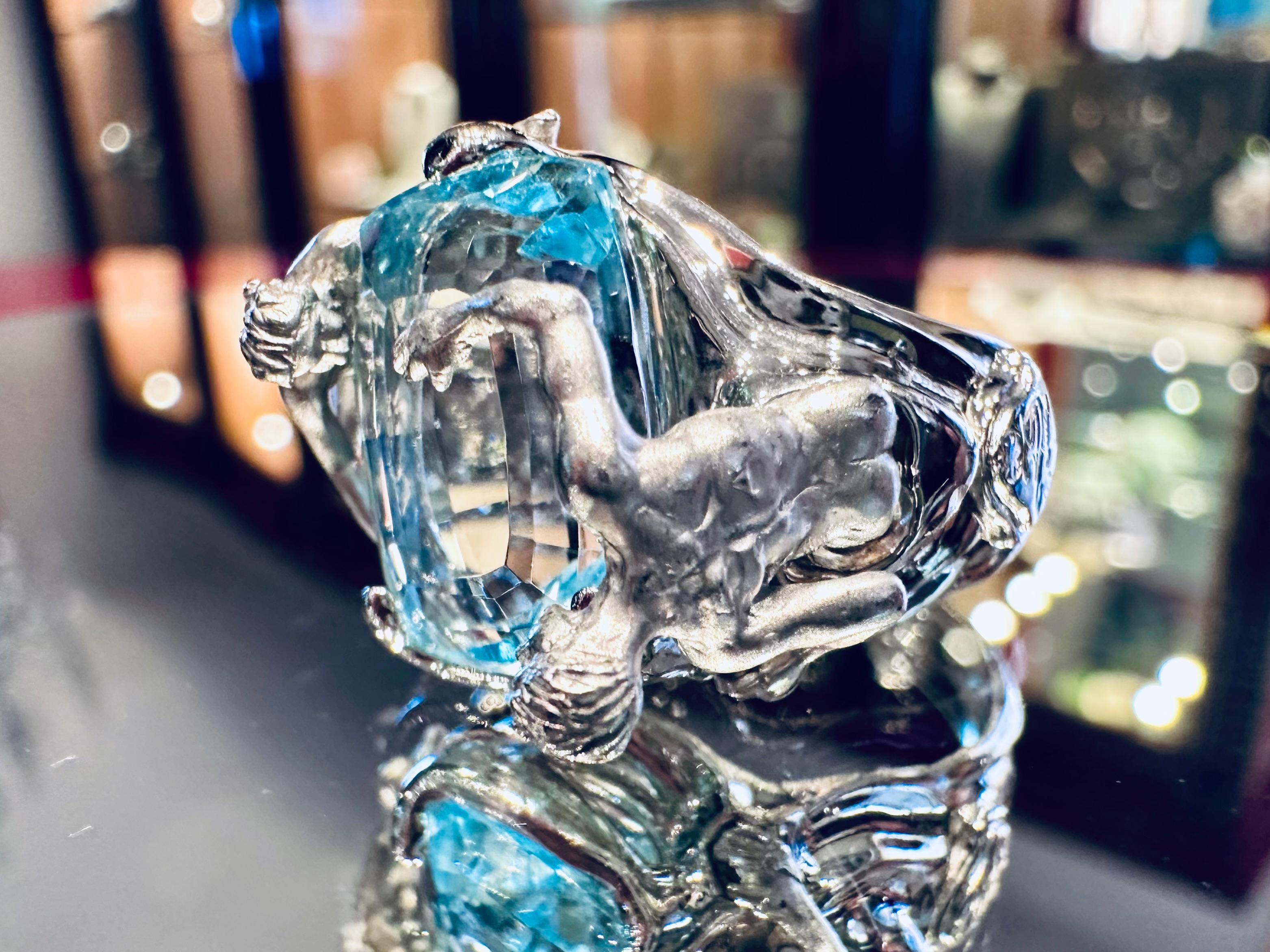 This extraordinary signed ring by Italian master goldsmith Ivo Spina is a striking and unique work of sculptural jewelry, crafted in solid 18-karat white gold (15.56 grams). At its heart lies a large, luminous blue topaz, expertly faceted to capture