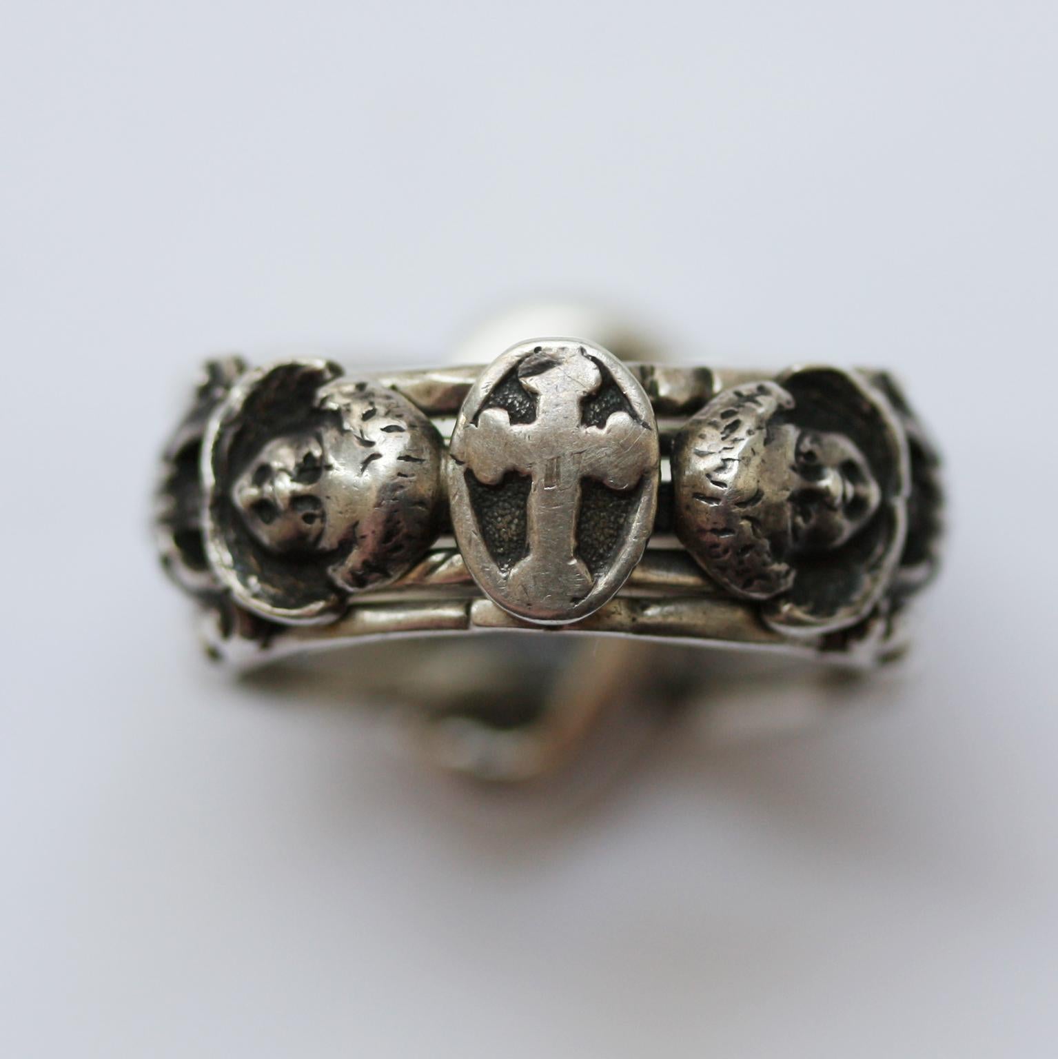 A silver neo-renaissance puzzle ring that consist of 5 bands that are intertwined at the back of the ring. In the middle is a cross and on each side of the cross is a winged angel, 19th century.

ring size: 19.25 mm. / 9 ¼ US
weight: 13.89 grams