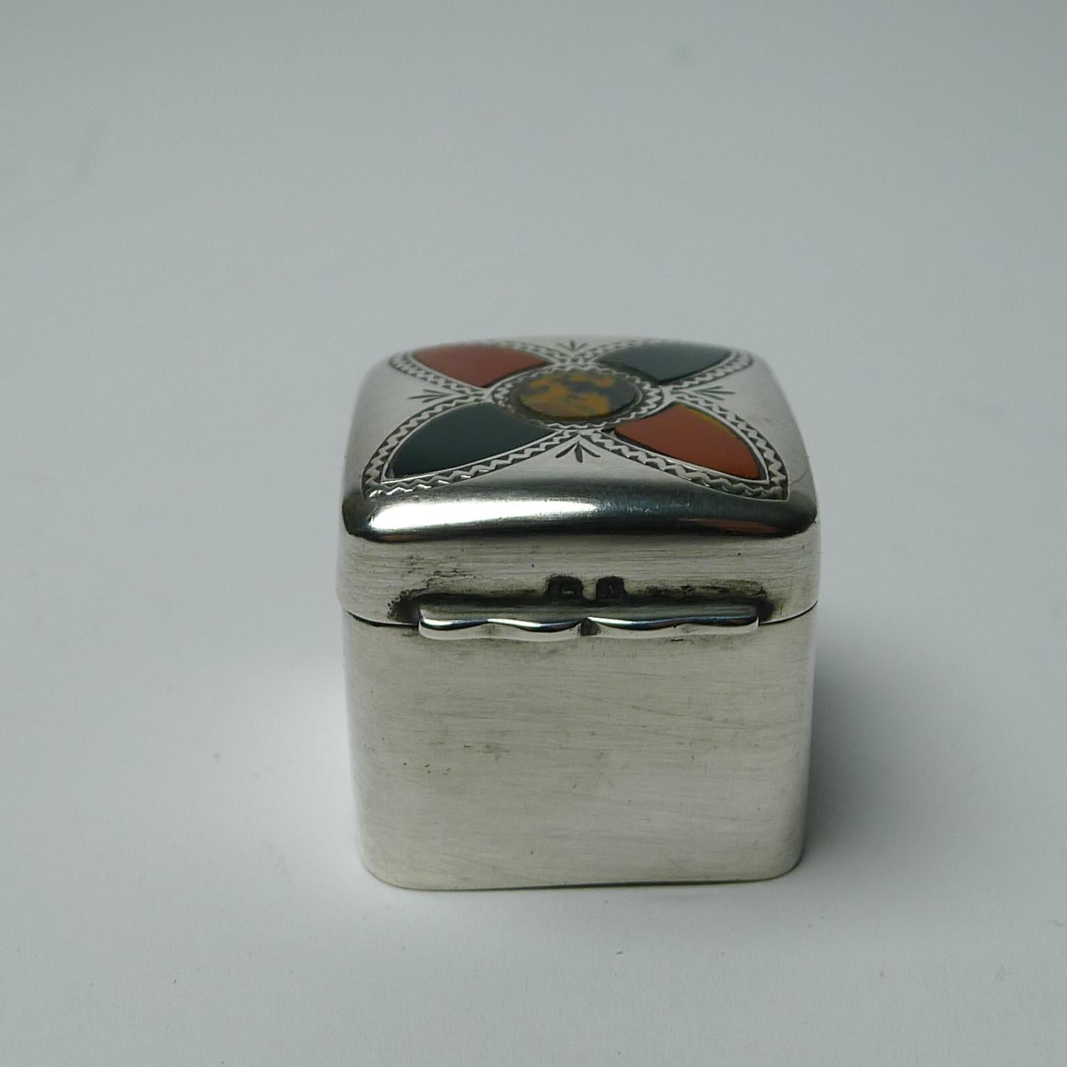 Un raro cofanetto quadrato in argento massiccio inglese con un cuscino intarsiato con pietre di agata color muschio verde, rosso e arancione.

Il coperchio incernierato si incastra bene e, usando l'ascensore sul davanti, si apre per rivelare