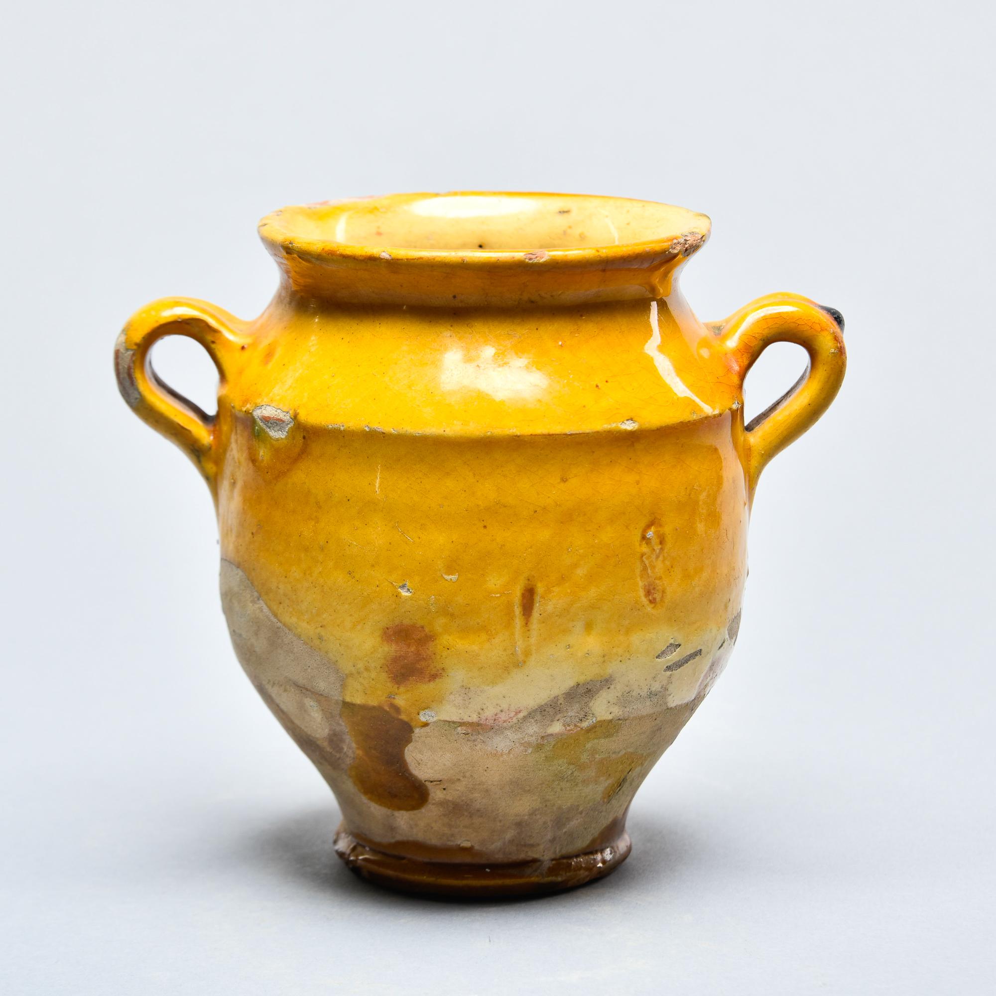Found in France, this French confit jar dates from approximately 1915. This piece stands 5.5” high and has the traditional form with a wide vessel body and two handles on the sides with a mustard-colored glaze on the outside top half and fully