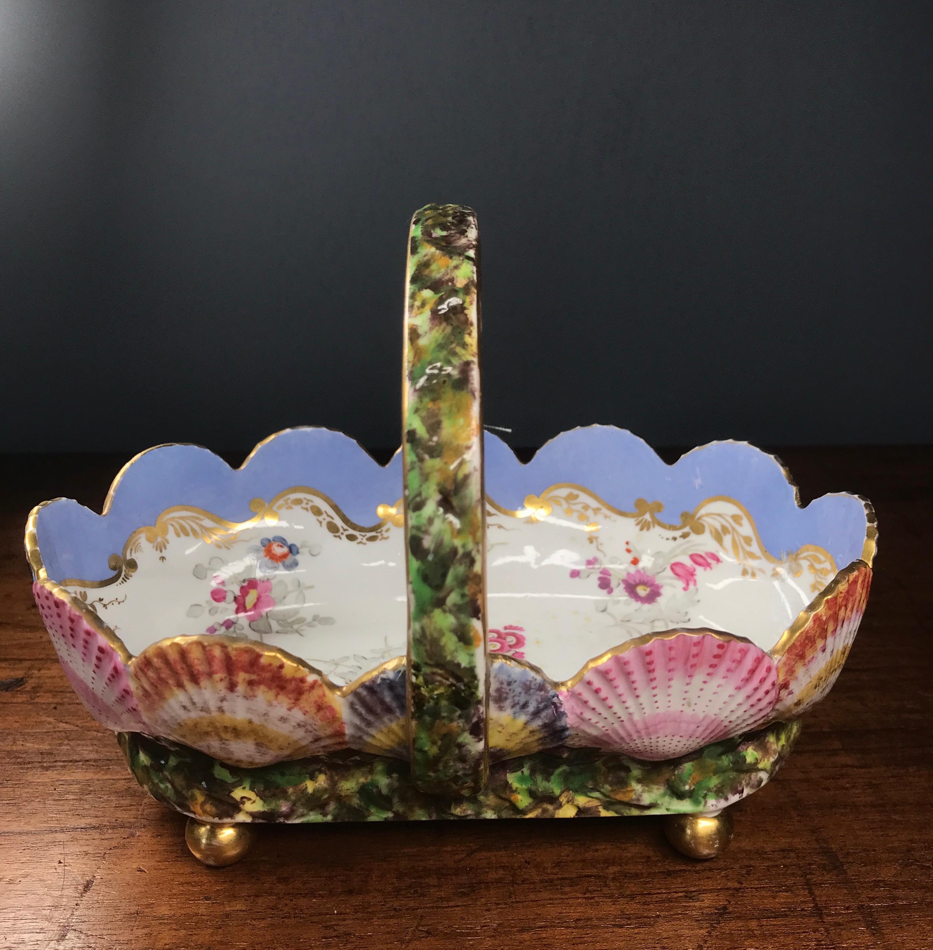 Rare Spode porcelain basket, formed as a series of linked Cockle Shells, each brightly coloured to the exterior & set in a bed of 'seaweed', a handle mid-way with the same green, on four gilt ball feet, the interior painted with a series of flower