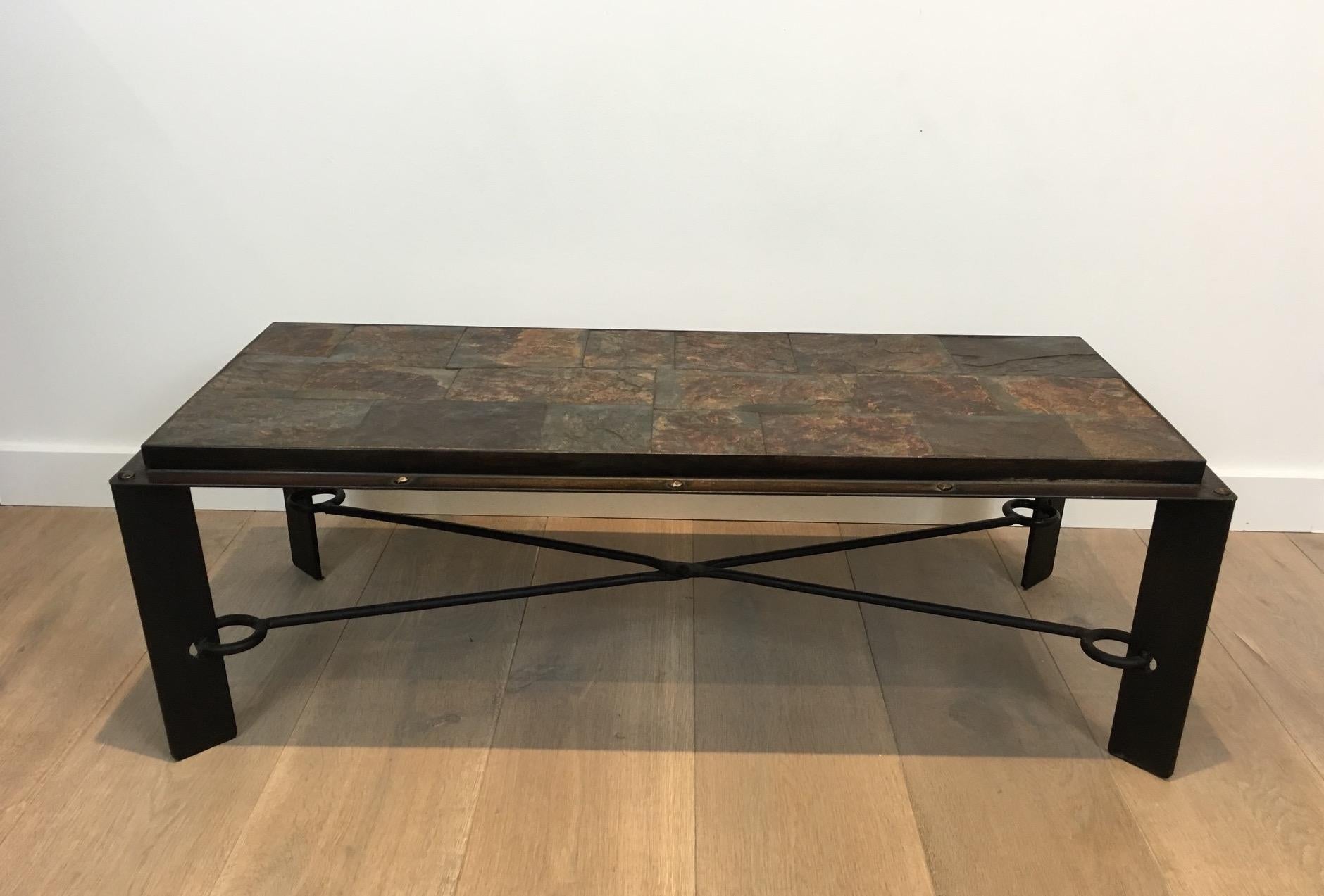 Cette table basse unique est composée d'une intéressante base en fer avec un châssis en croix fixé aux pieds par un grand anneau. Le plateau est constitué d'une belle pierre de lave entourée d'un épais cadre en acier avec de gros rivets. Il s'agit