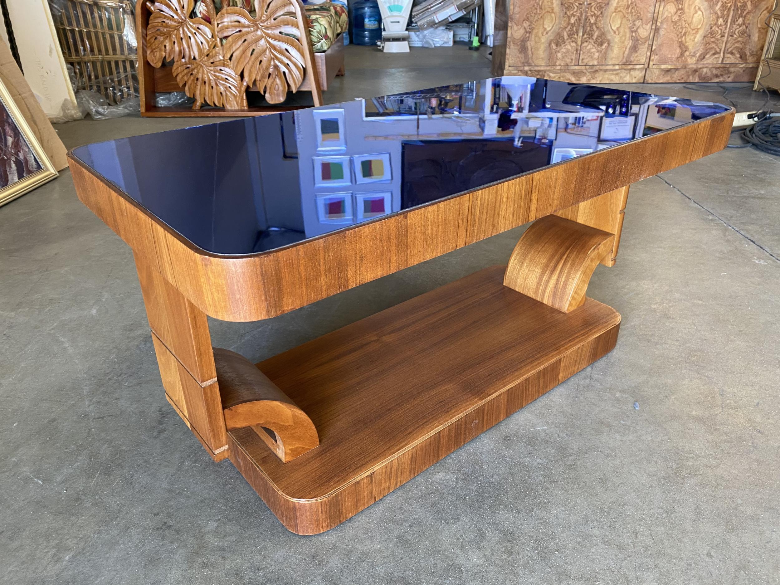 Original Streamline Art Deco mahogany coffee table w/ cobalt glass top featuring an hourglass base. 

 
