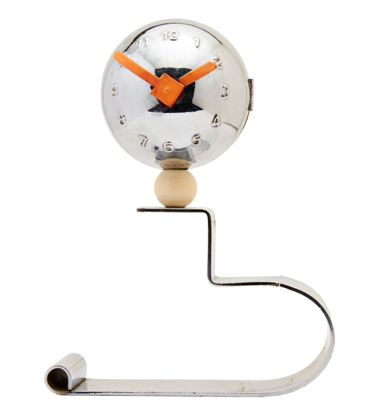 This rare and stunning German Art Deco ball clock features embossed numerals with red enameled geometric hands. The spherical case sits atop a cream enameled sphere that is in turn mounted to a free form, asymmetrical chrome ribbon stand. There is