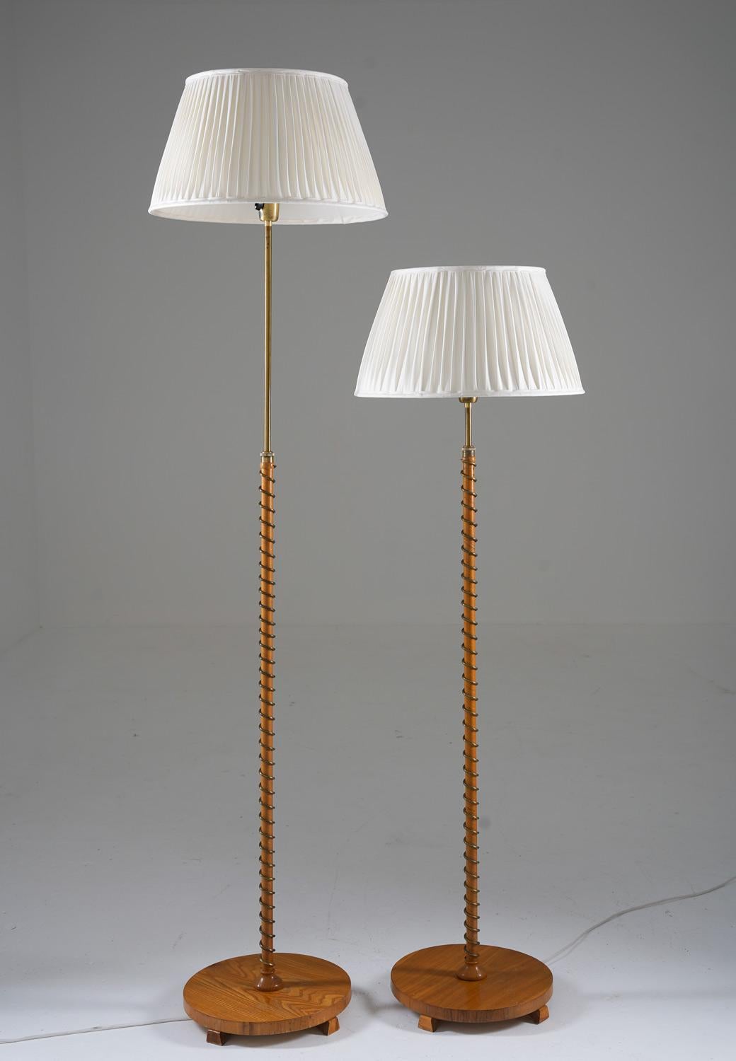 Beautiful floor lamps, manufactured in Sweden ca 1940.

These rare floor lamps consist of a brass pole, webbed in elmwood with a brass spiral around it. The pole is supported by a large wooden foot.
The height is adjustable from 140cm (55