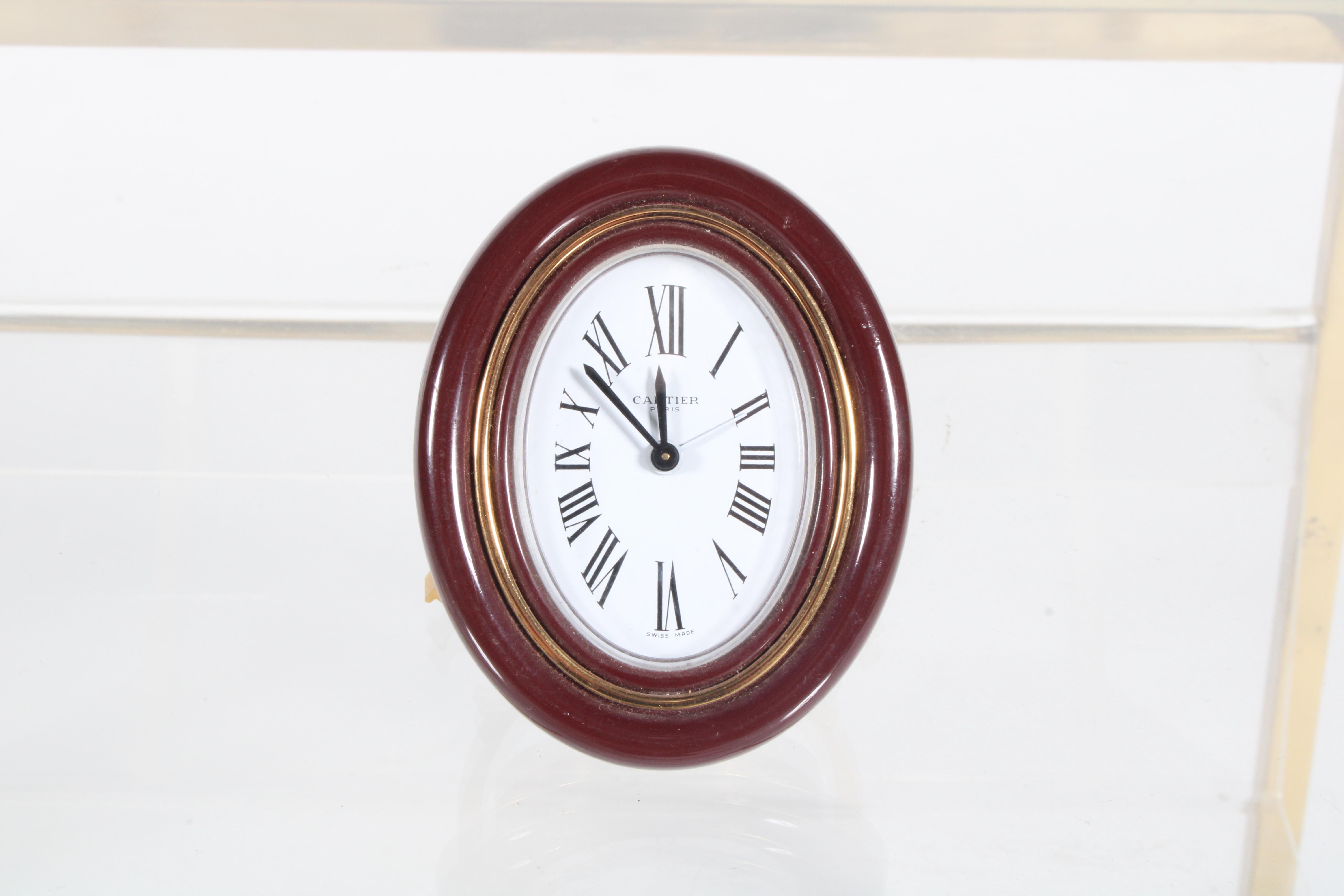 A charming original desk clock from the iconic brand Cartier. This pocket size desk clock is presented in superb vintage condition. In oval form with white face and Roman numerals, the gold plated back is stamped and engraved with the makers name