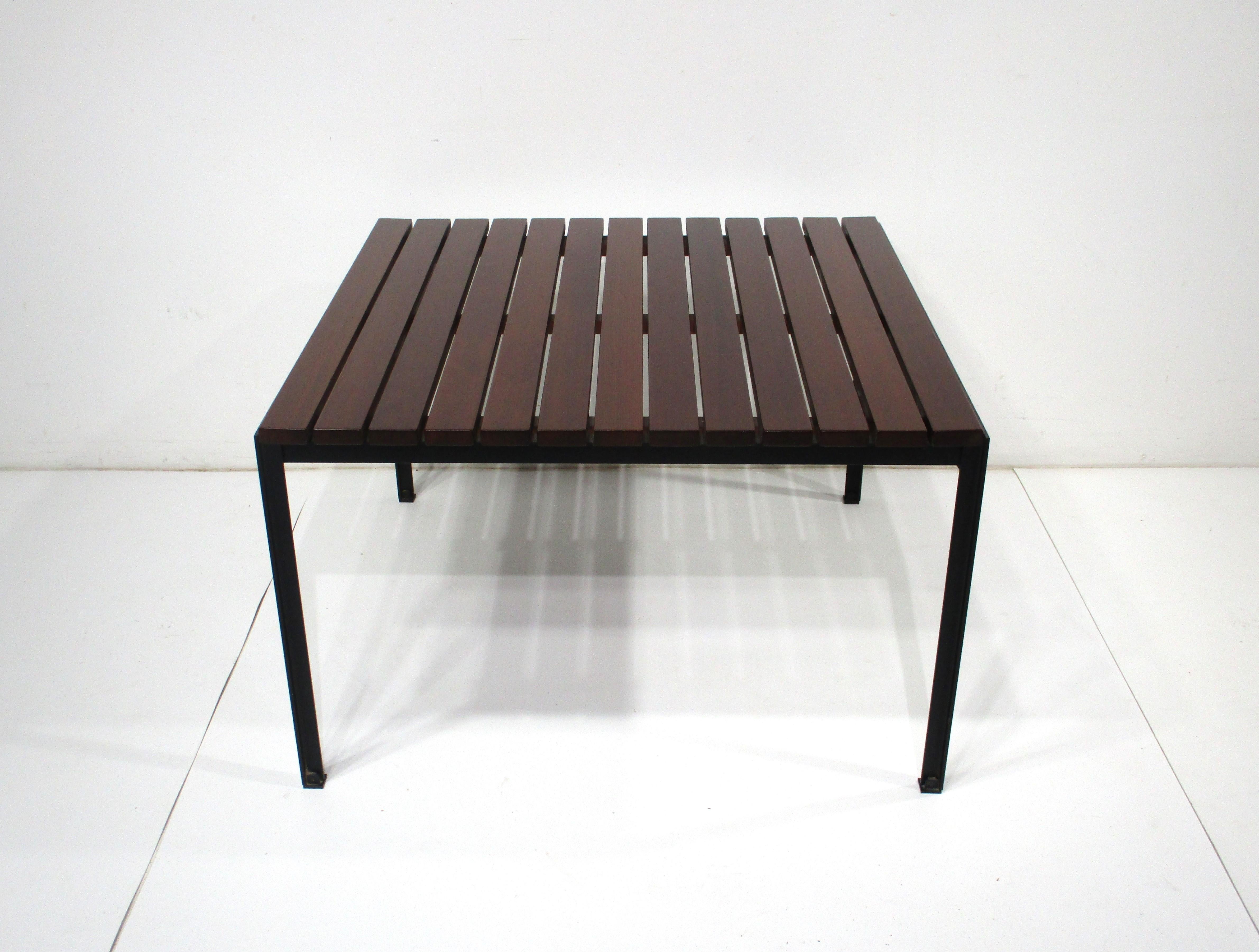 A rare dark slat redwood square coffee table having a black metal base that's been angle formed as in it's given name T Angle table . This hard to source form was designed by Florence Knoll in the late 1950's and retains the early fabric big K label