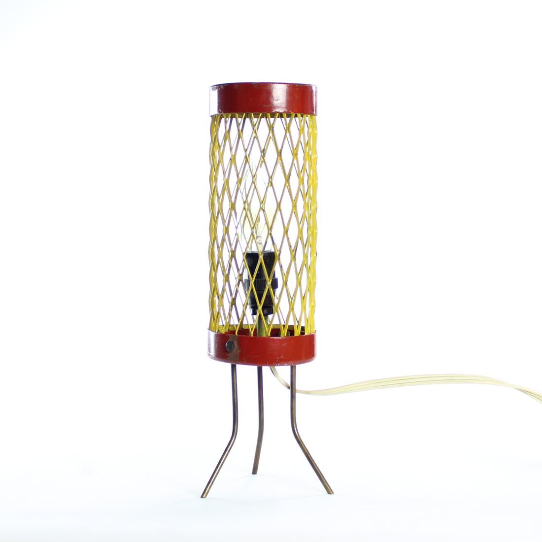Rare table lamp produced in Czechoslovakia in 1950s. The lamp is stands on three elegant metal legs. The shield consists of a strong steel mash in yellow color. The top and bottom rings holding the mash are also made of steel, in bordeaux color. The