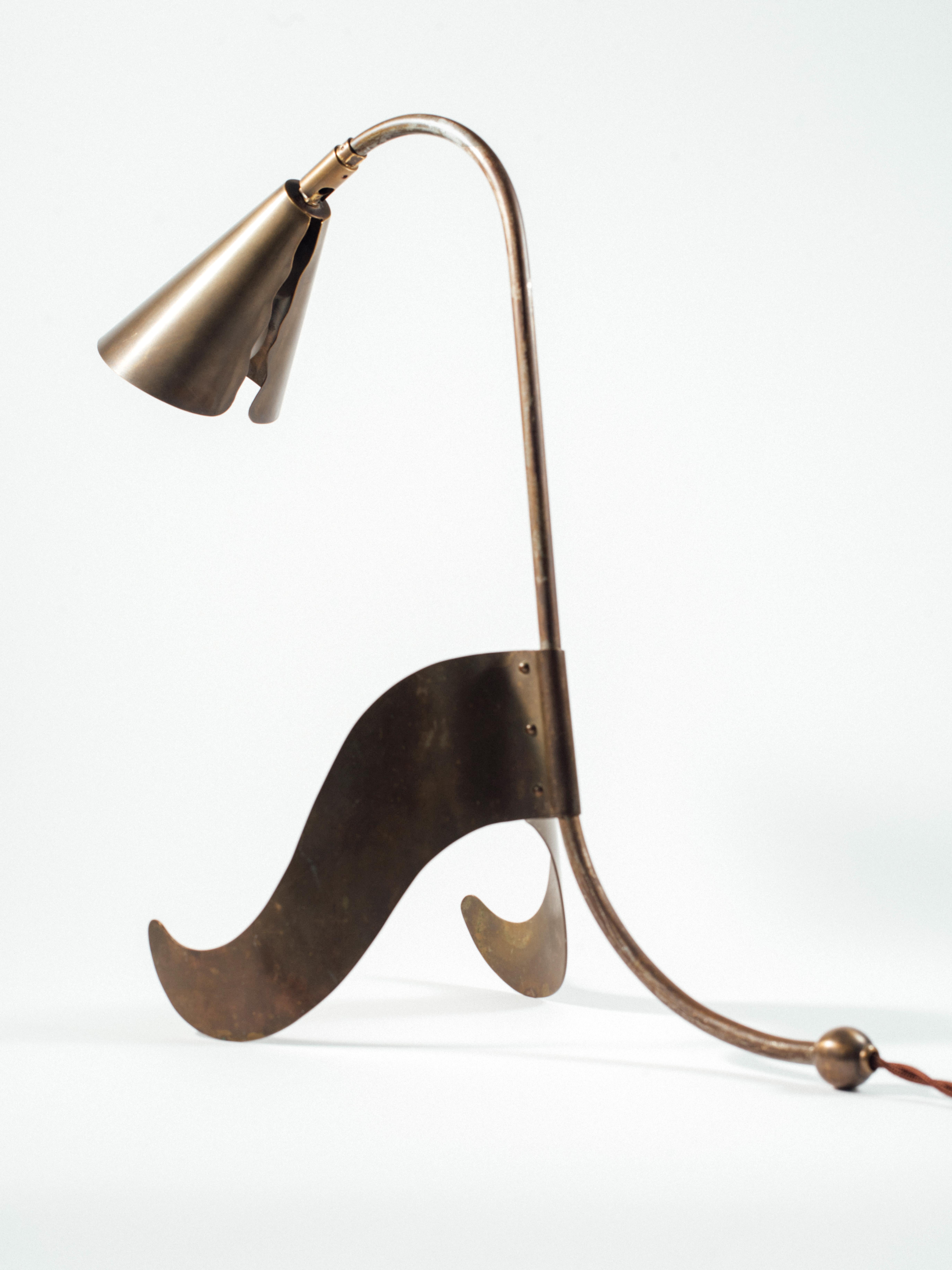 A desk lamp with a lyrically bent frame in patinated steel and a conical, articulating shade, front legs and spherical counterweight, all in solid, patinated brass. The sinuous cut-away section at the rear of the light shade both mimics the shape of