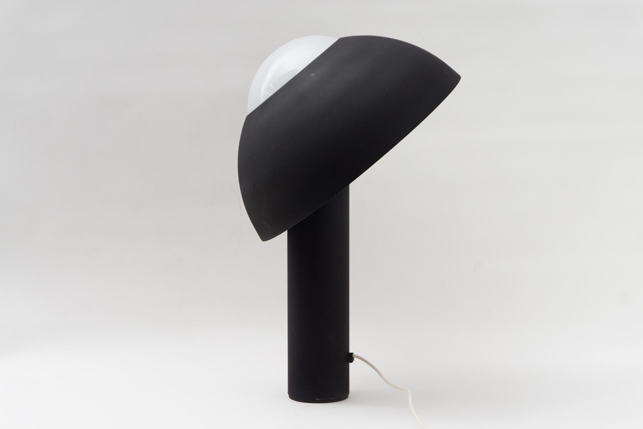 This table lamp made of metal is an extraordinary piece of lighting. It has a solid and playful quality, through it's shade being removable and adjustable in position. Coating in matte black structural lacquer, round lamp made of satined glass.