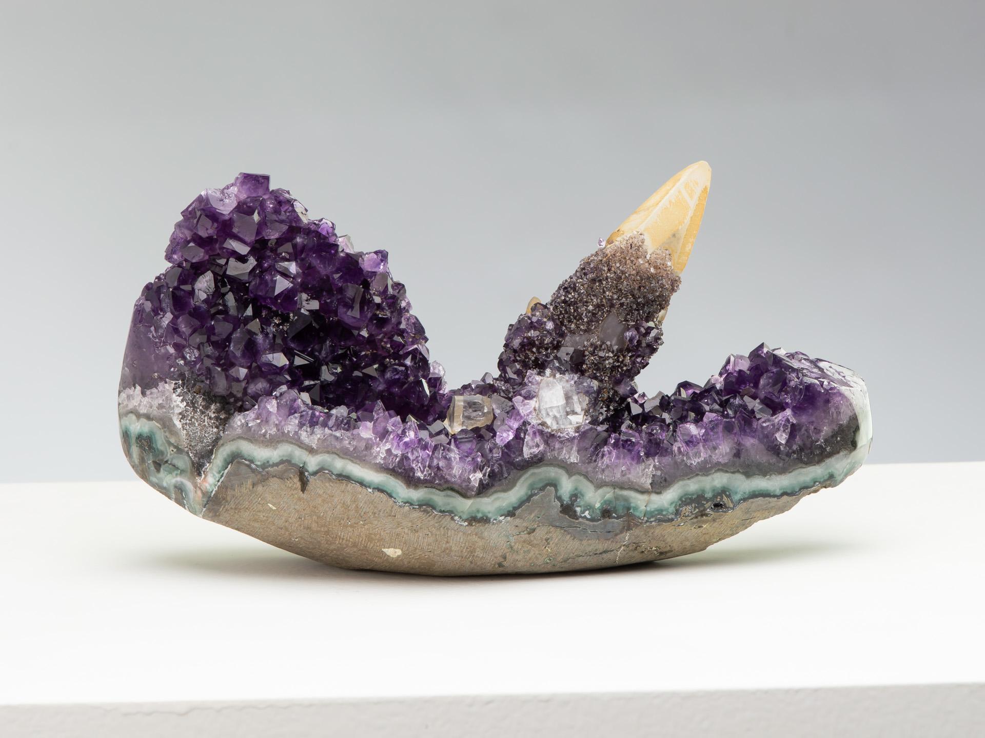 A very rare and exquisite table-top amethyst formation. The long fromation preserves a prominent golden calcite crystal on a bed of deep purple amethyst and is particularly sculptural. The calcite is itself covered in rare goethite and white quartz,