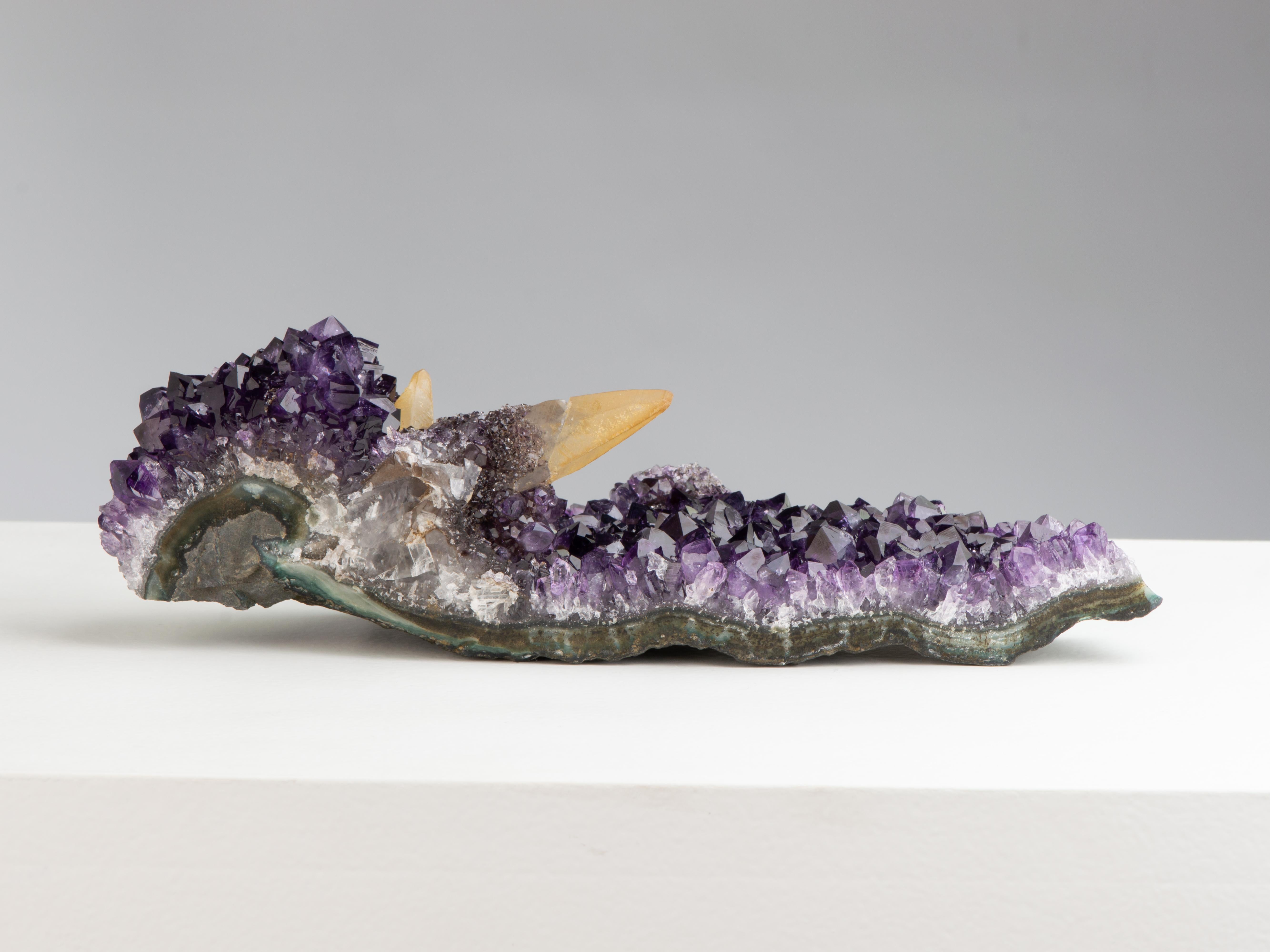 A very rare and exquisite table-top amethyst formation. The long formation preserves prominent golden calcites crystal on a bed of deep purple amethyst and is particularly sculptural. The calcites are covered in rare goethite and white quartz,