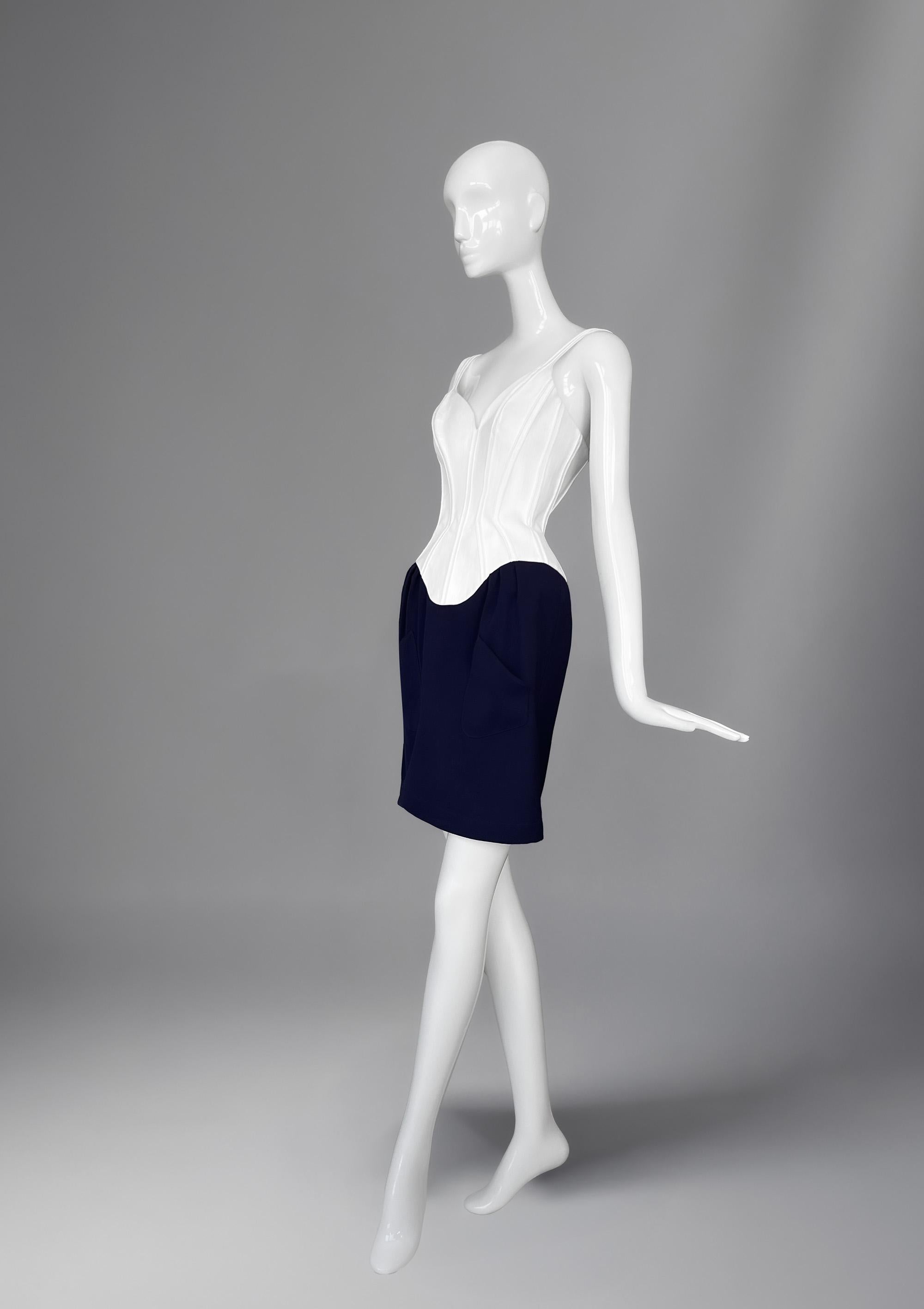 La robe corset de Thierry Mugler est un chef-d'œuvre sculptural. Cette robe allie la coupe au cordeau de Mugler à une allure sensuelle. Le corsage, conçu comme un corset blanc structuré, cintre la taille avec une précision presque impossible, créant