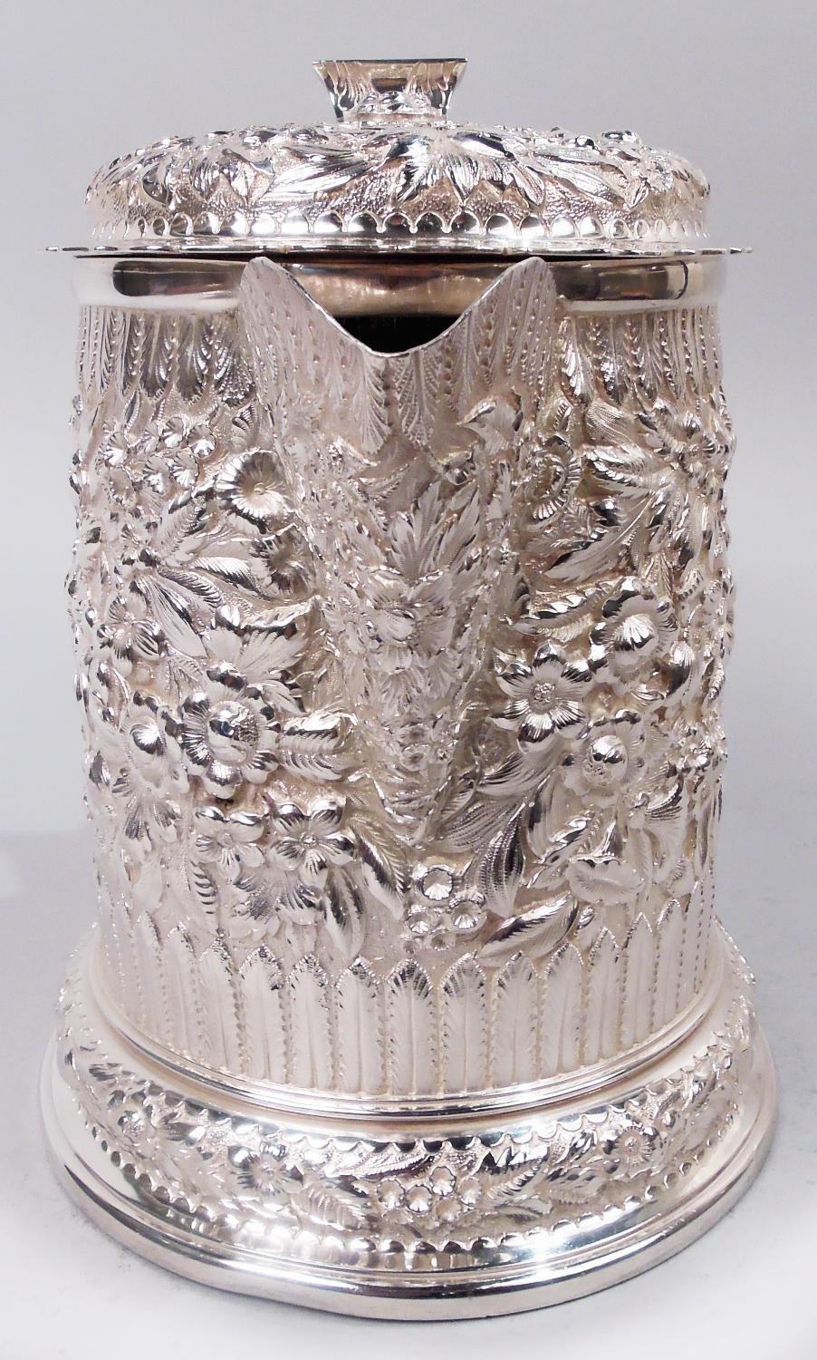 Rara jarra clásica victoriana de plata de ley. Fabricado por Tiffany & Co. en Nueva York, hacia 1875. Forma de tambor con caño en V de gran capacidad y base con faldón. Tapa abisagrada y alzada con capullo de flor central que irradia una hoja y un