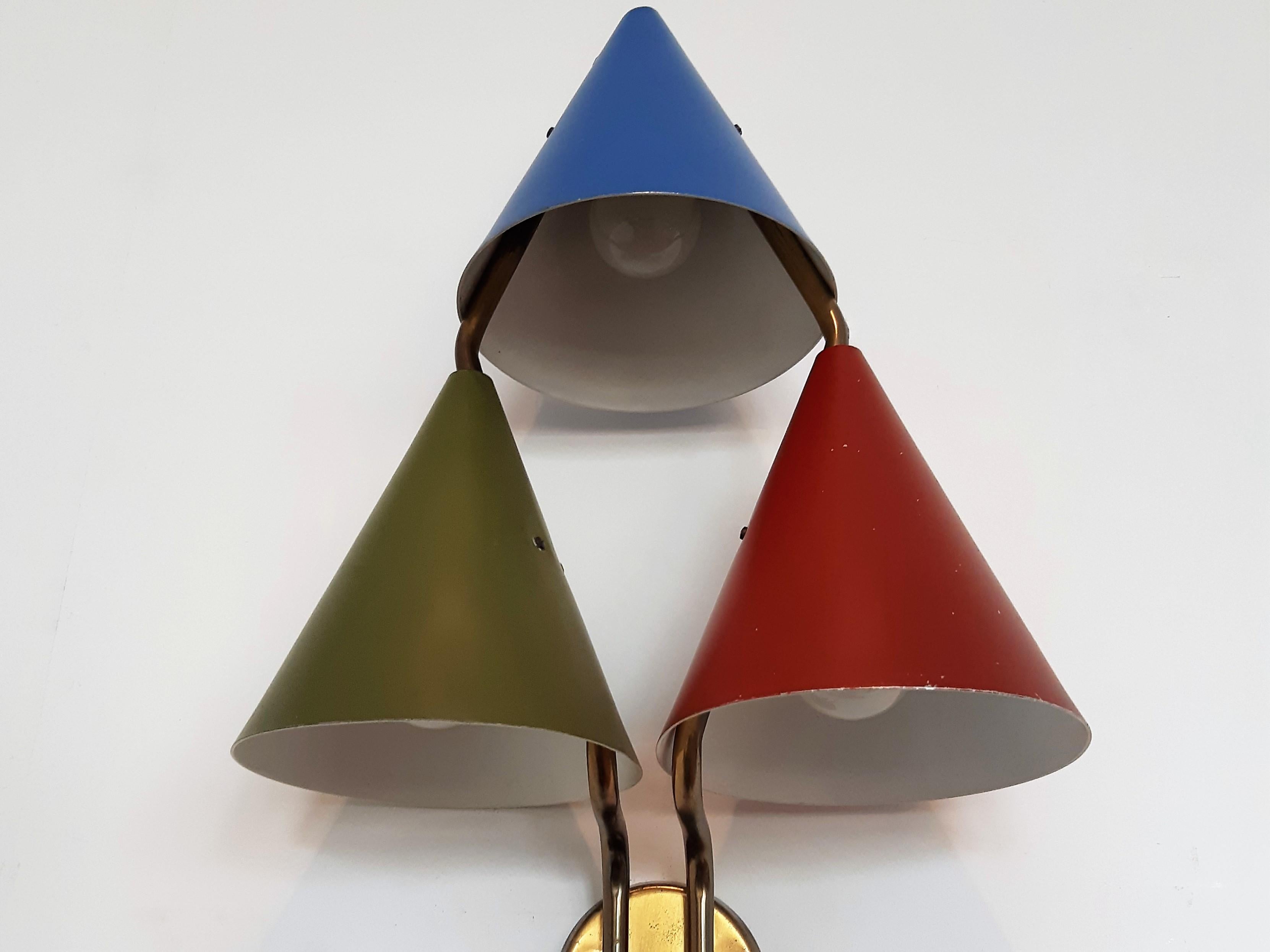 This highly rare wall sconce, model Mosaik, was designed by Bent Karlby in Denmark in the 1950's. It has 3 conic shades in blue, green and red, attached to a brass frame. The conic shades were also applied to pendant lamp variants, however this wall