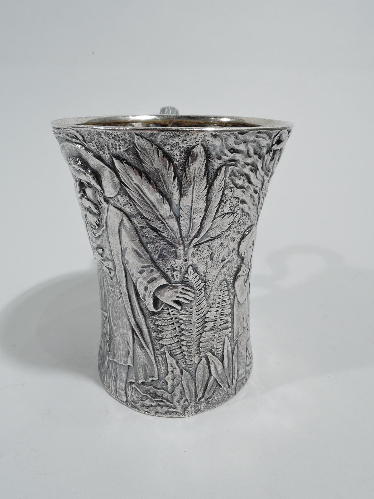 Unusual sterling silver baby cup. Made by Tiffany & Co. in New York. Tall and waisted with dense low-relief frieze depicting 2 boys, one holding a genie lamp and the other heaving a case out of the ground, as well as 2 magical or divine figures of