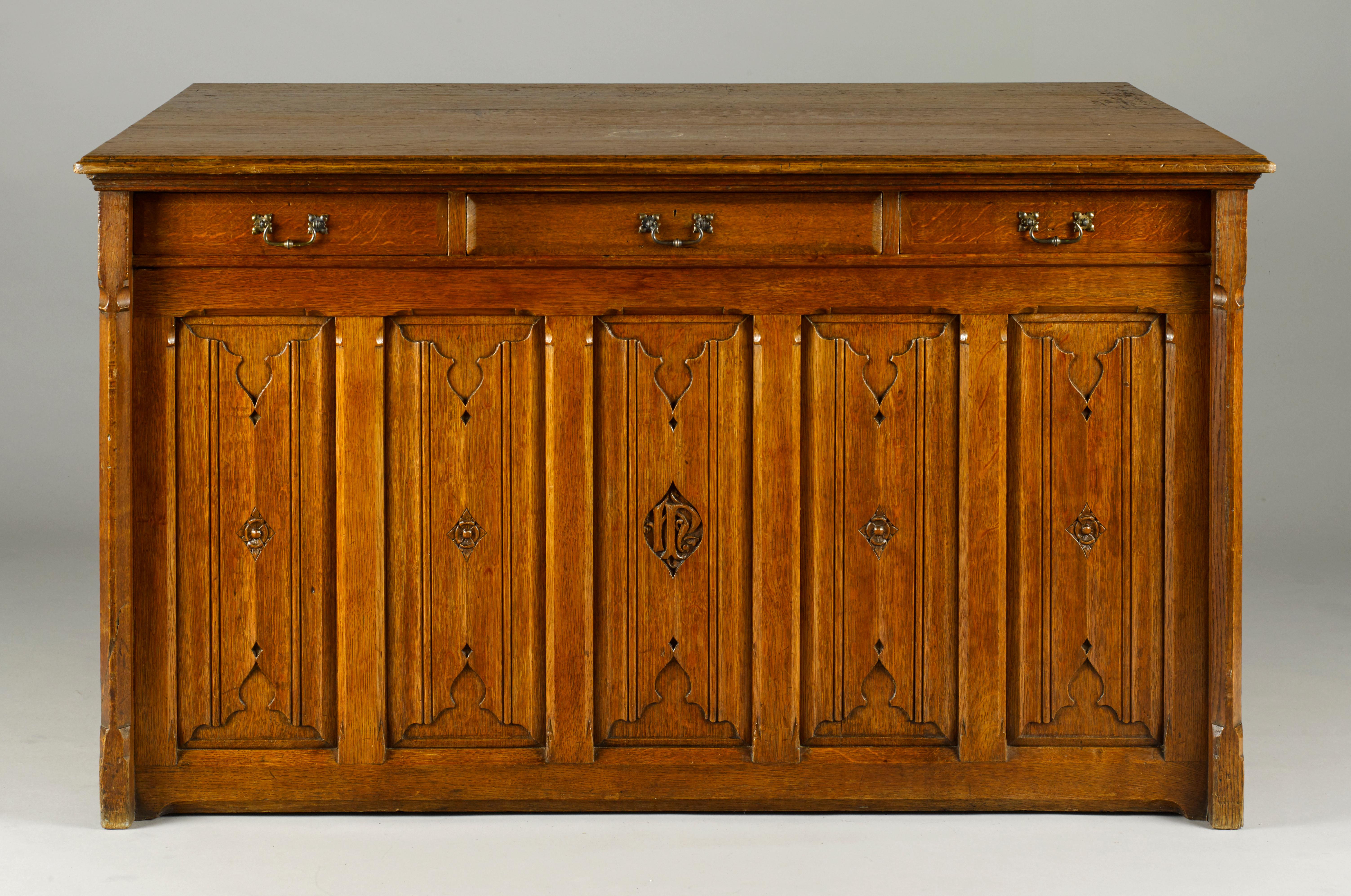 A neo-gothic mid-19th century library plan chest having an arrangement of eleven short and three long drawers to one side, the other side with three short drawers above gothic style linen fold panelling, centred with the carved monogram ‘HP’,