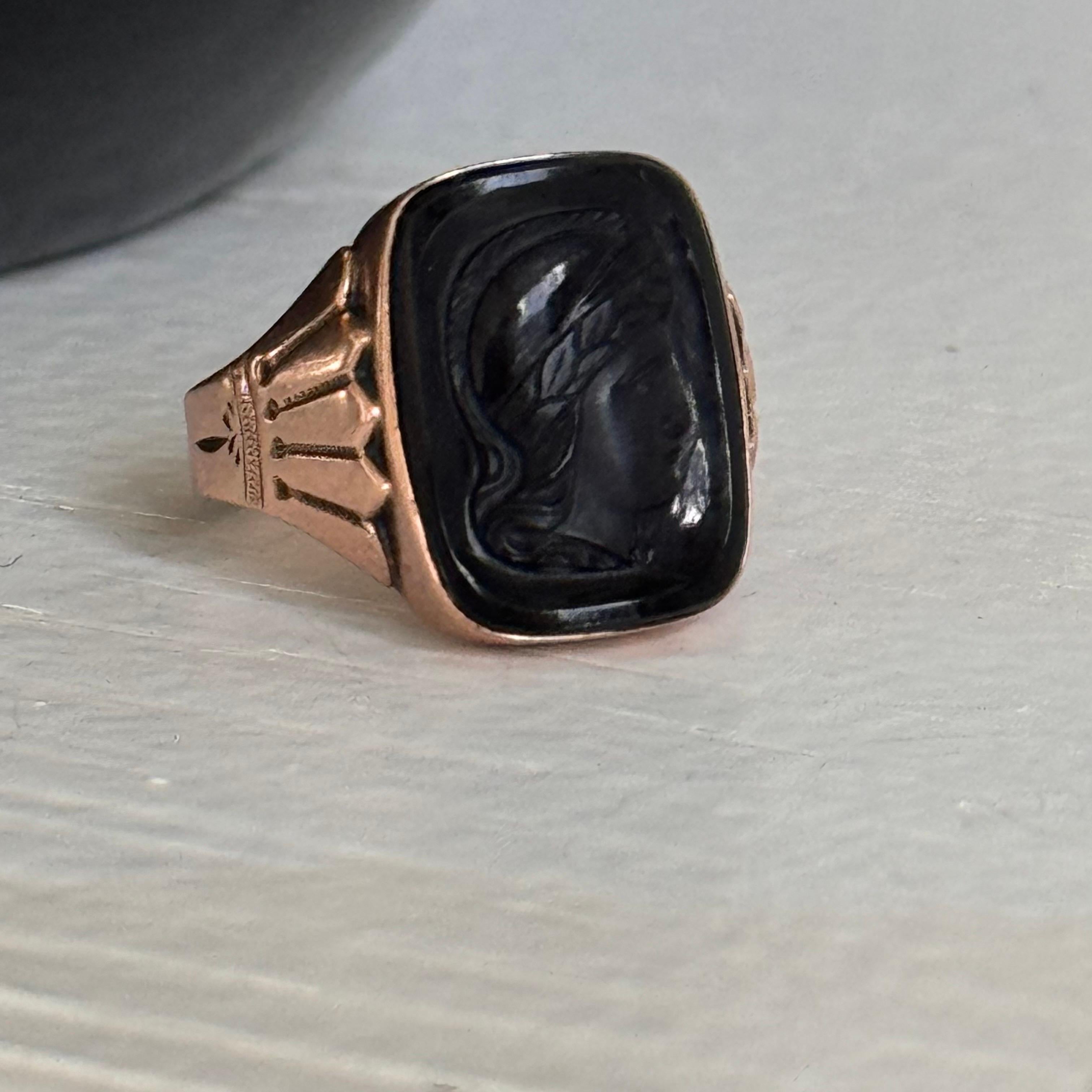 Rare and stunning Victorian signet ring is crafted from warm rose gold, featuring a cushion-shaped onyx that is deeply engraved with a profile of a head, showcasing the exceptional artistry of the period. The bold yet elegant design is a testament