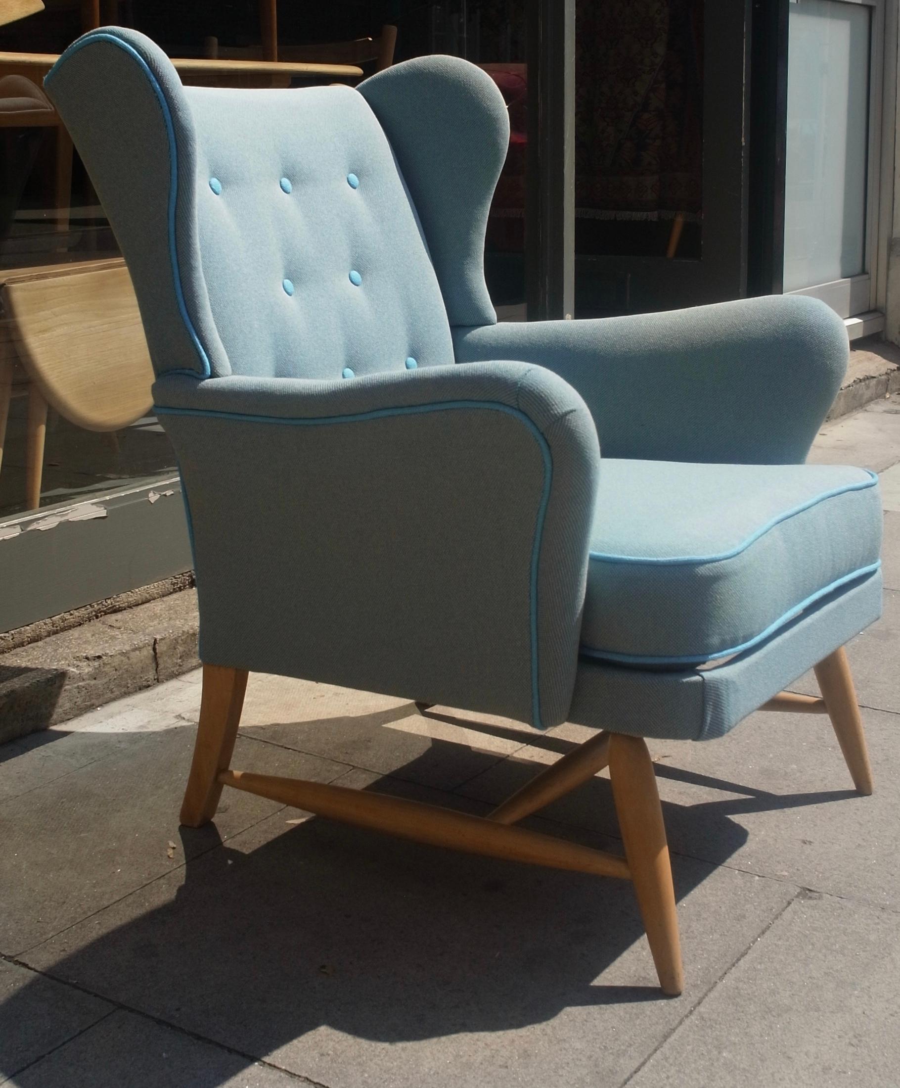 A very rare, comfortable and stylish vintage 1950s Ercol wingback armchair, newly reupholstered in a light blue 100% wool 'steel-cut' textile with a contrasting blue piping and buttons, on an external Beech framed base. This armchair is in excellent