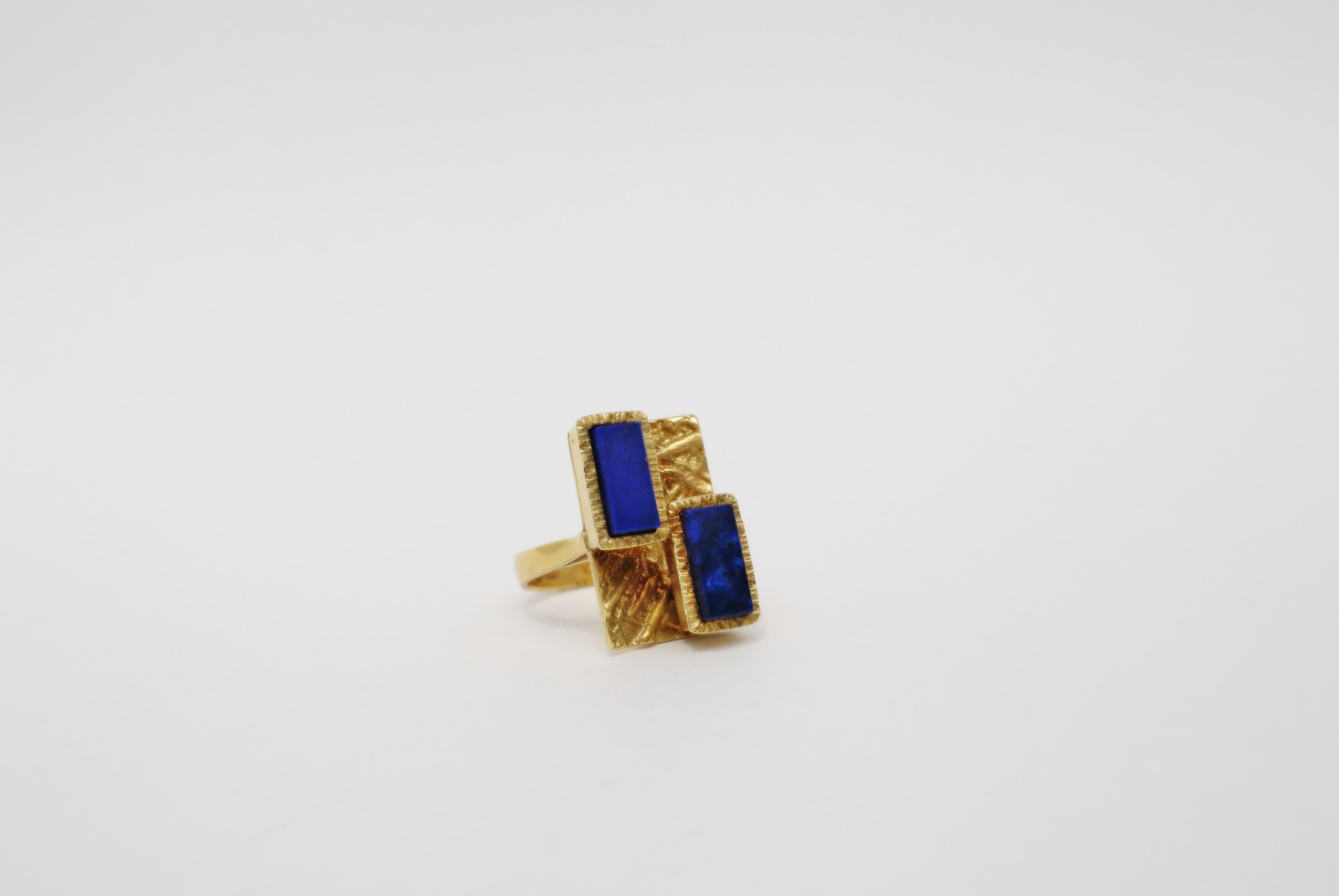 This is a rare vintage Cartier 18k gold ring with a geometric design. The ring features two rectangular squares with lapis lazuli as the main stones. The bezel setting style is used to hold the gemstones in place. The ring is made of yellow gold