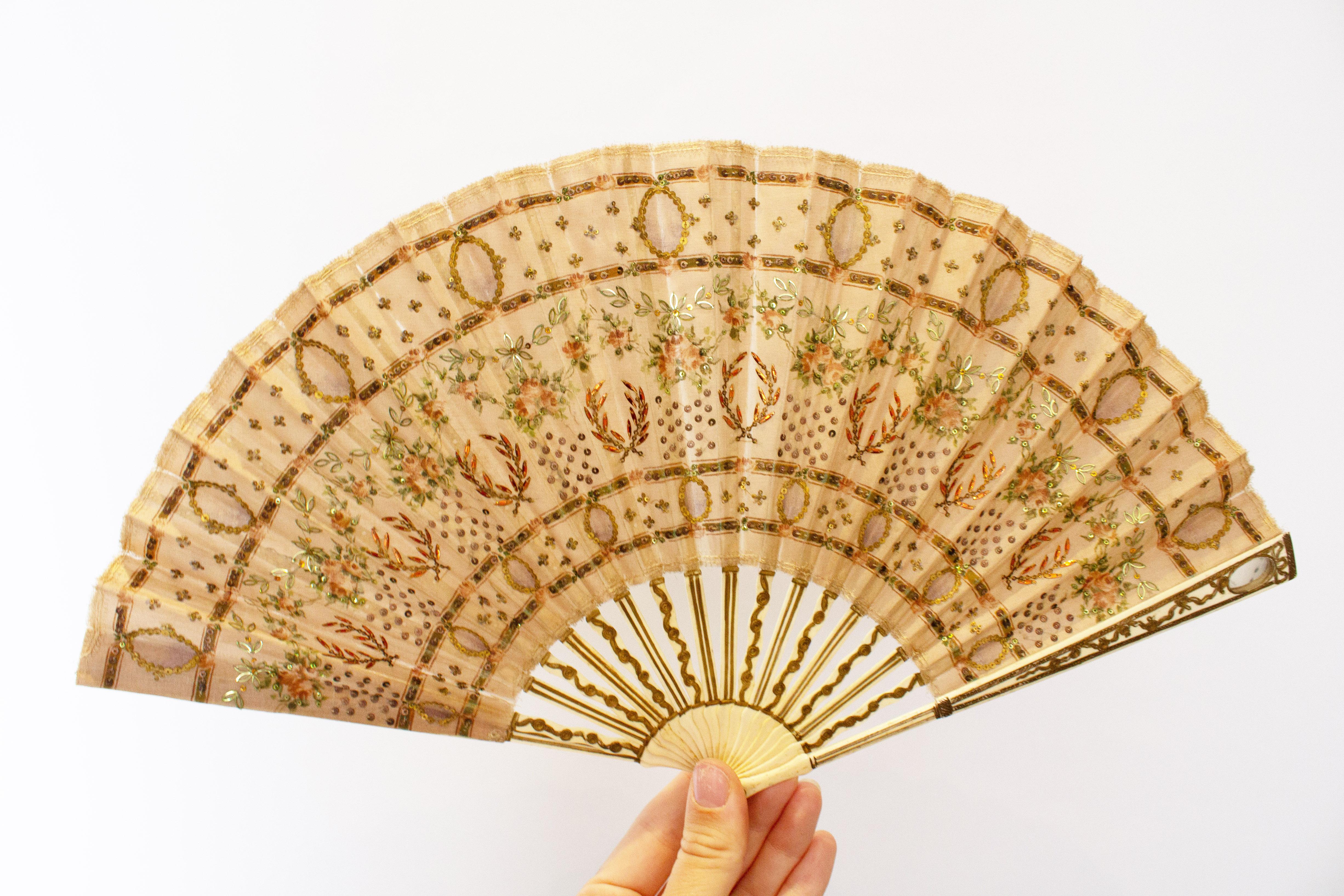 An attractive and rare vintage fan. The ivory sticks and handle are decorated with 'gold', and one side has a charming small mirror. The fabric is decorated with sequins and beads. Maximum width 16'', height 9''
