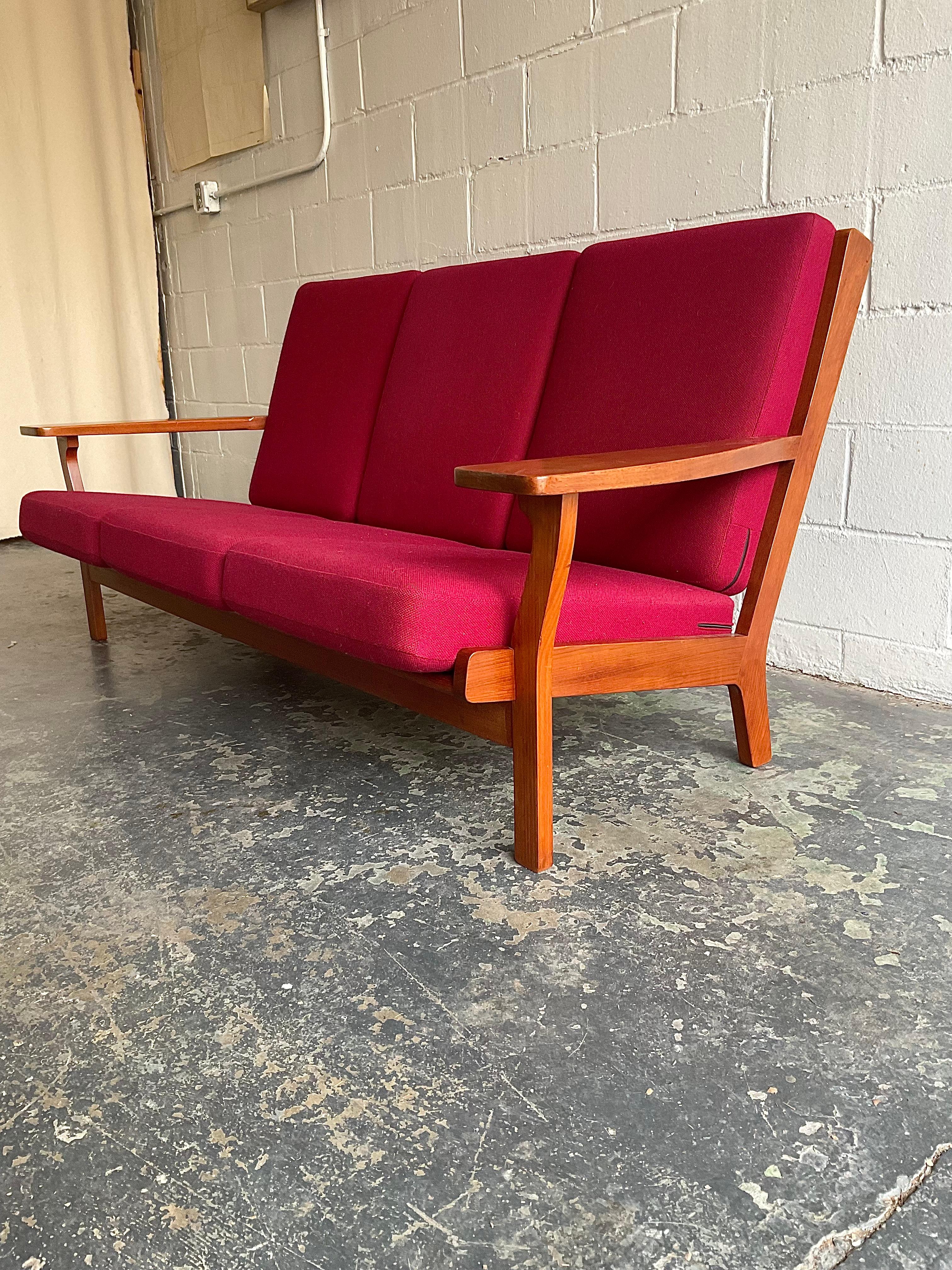 Elegant and commodious, here we have a rare example of Wegner’s celebrated GE-330/3A three seat sofa in carved teak frame and light burgundy boiled wool upholstery with original spring back and seat cushions. This example remains in very good