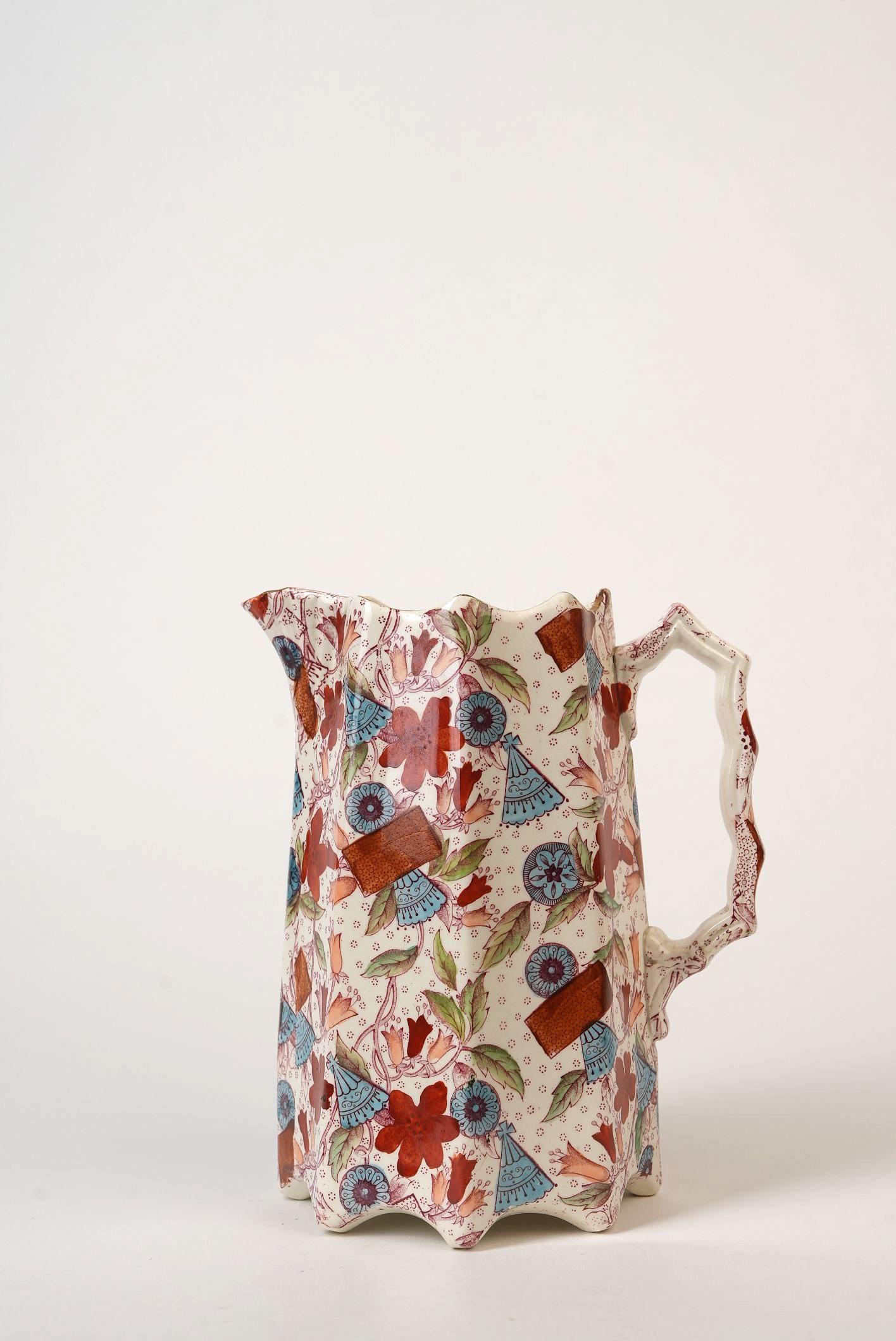 A striking example of East-meets-West design, this vintage Imari-style pitcher features a richly decorated surface teeming with hand-painted florals, geometric medallions, and fan motifs in a vibrant palette of rust red, cobalt blue, and soft green.