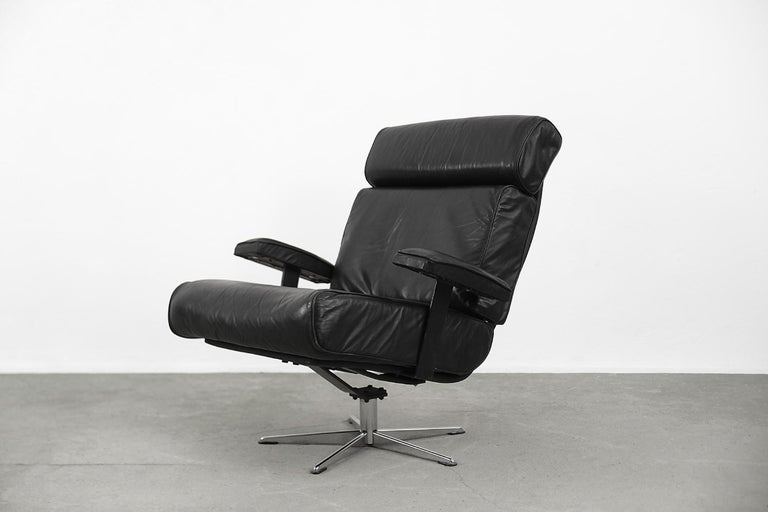 This office swivel armchair was manufactured in the Germany during the 1960s. The frame is made from metal. The chair is upholstered in real soft leather in black color. The headrest has a leather slack overlap and is clasped on the back. It is a
