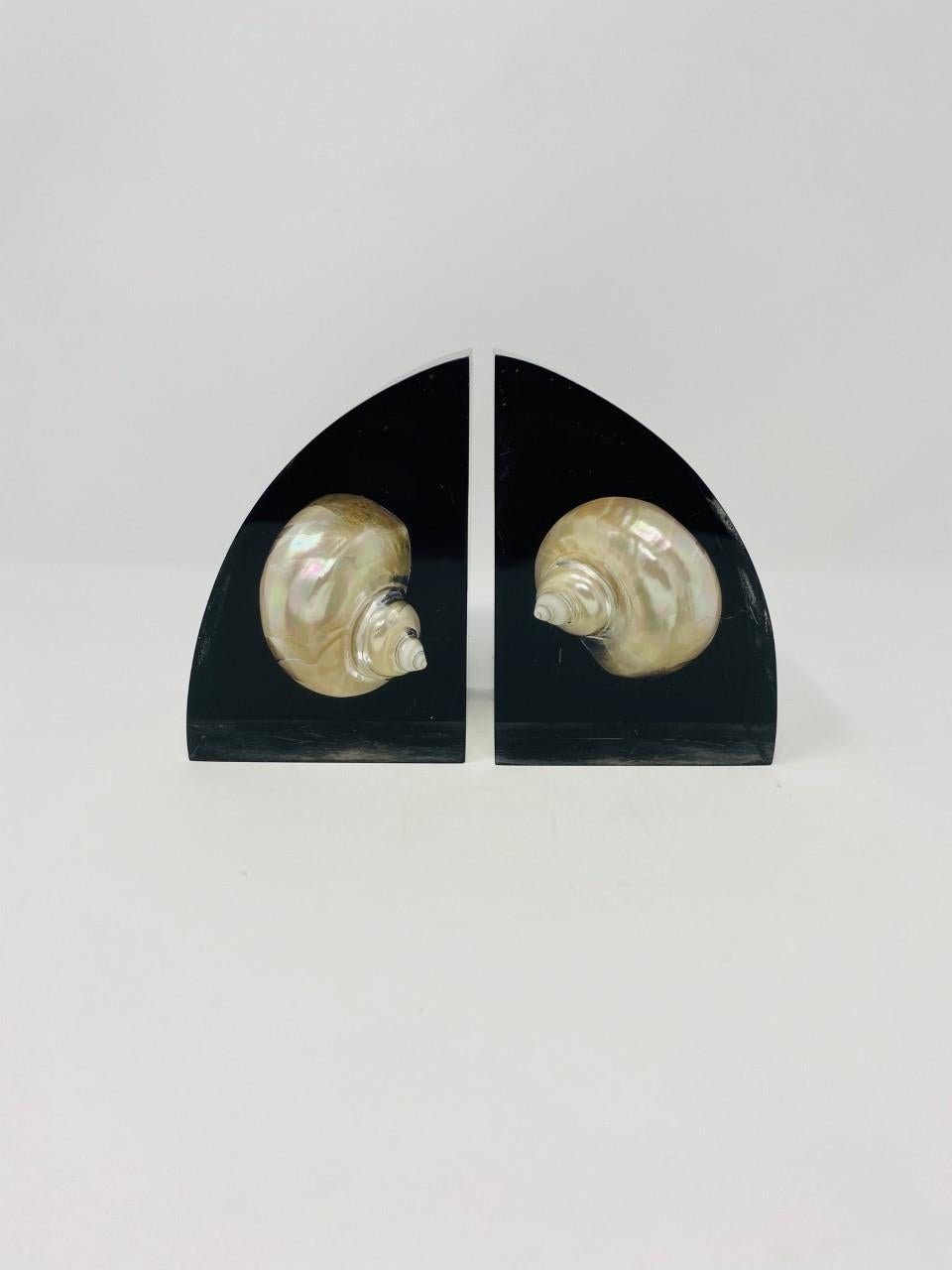 Beautiful vintage mid century lucite bookends with embedded shell. These 1960s gems are glamorous, lustrous and enigmatic. Two perfectly proportioned seashell specimens float in lucite that projects them in a dark background. The iridescent natural