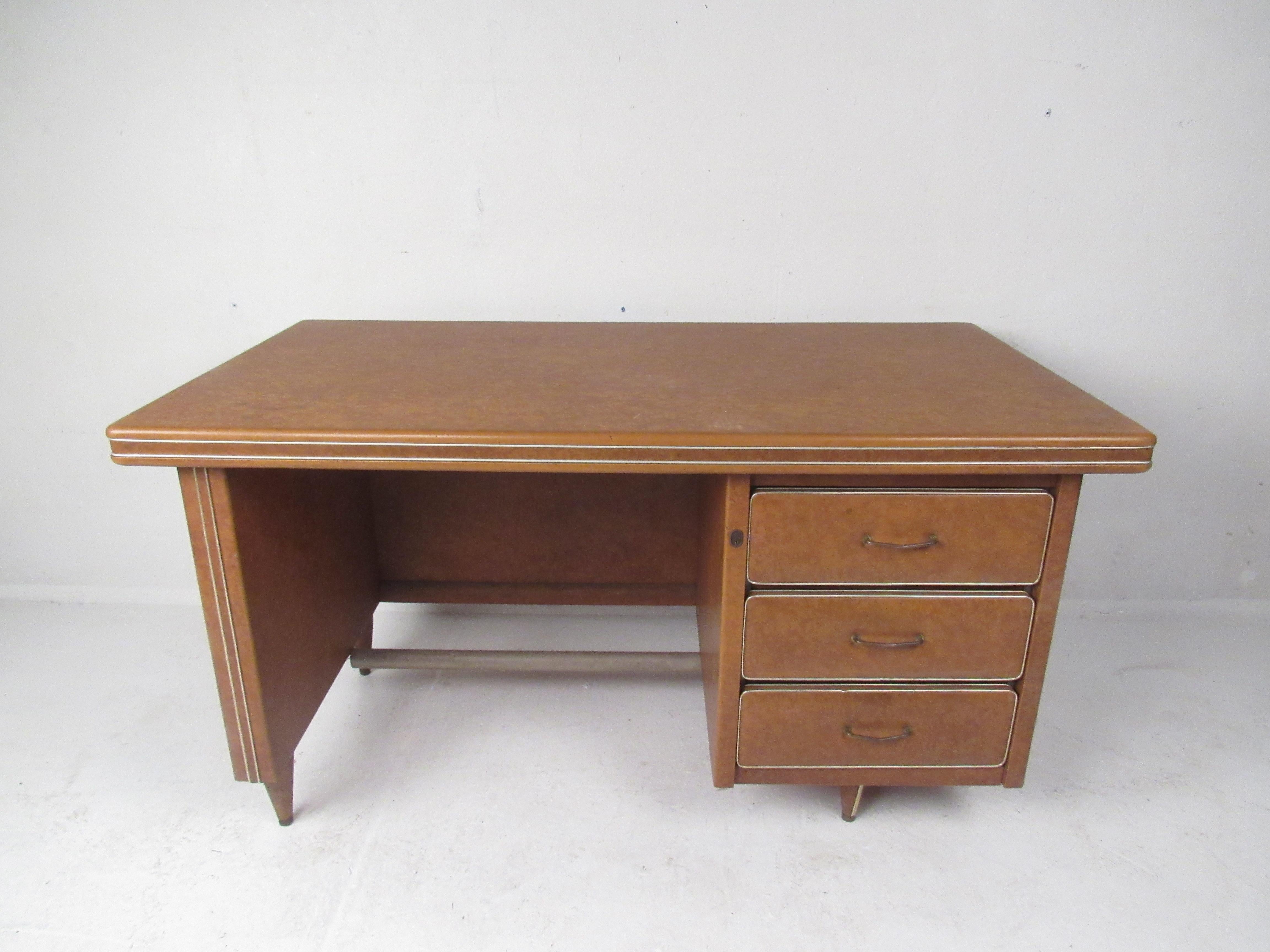 This beautiful Mid-Century Modern desk is covered in a smooth synthetic material with metal trim wrapped around the top. An unusual design with three hefty drawers ensuring plenty of room for storage. The sculpted brass drawer pulls, stubby legs,