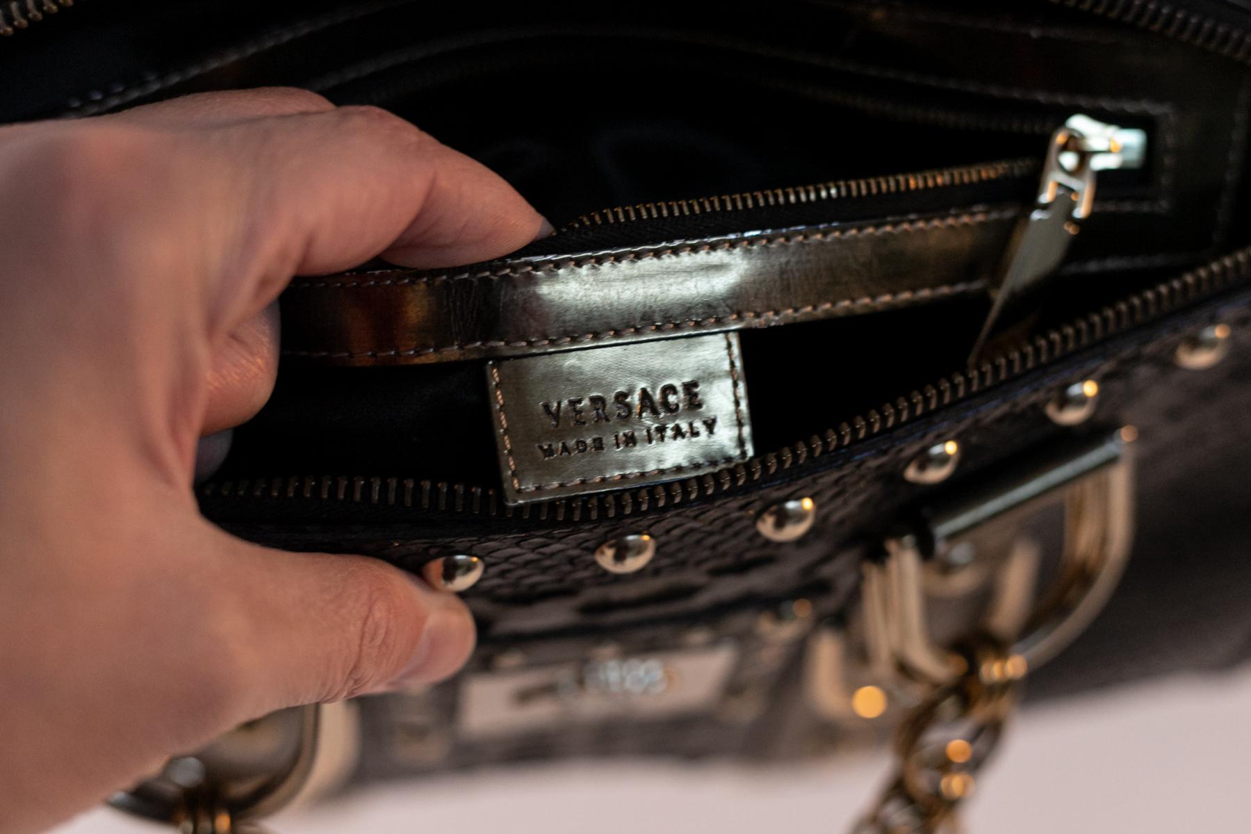 Exzentrische Lederhandtasche, entworfen vom großen Gianni Versace in den 1970er Jahren.
Die Tasche ist eine Handtasche aus schwarzem Leder mit eleganten Goldnieten.
Die Ärmel sehen aus wie auffällige goldene Ketten, sehr exzentrisch. Die Tasche hat