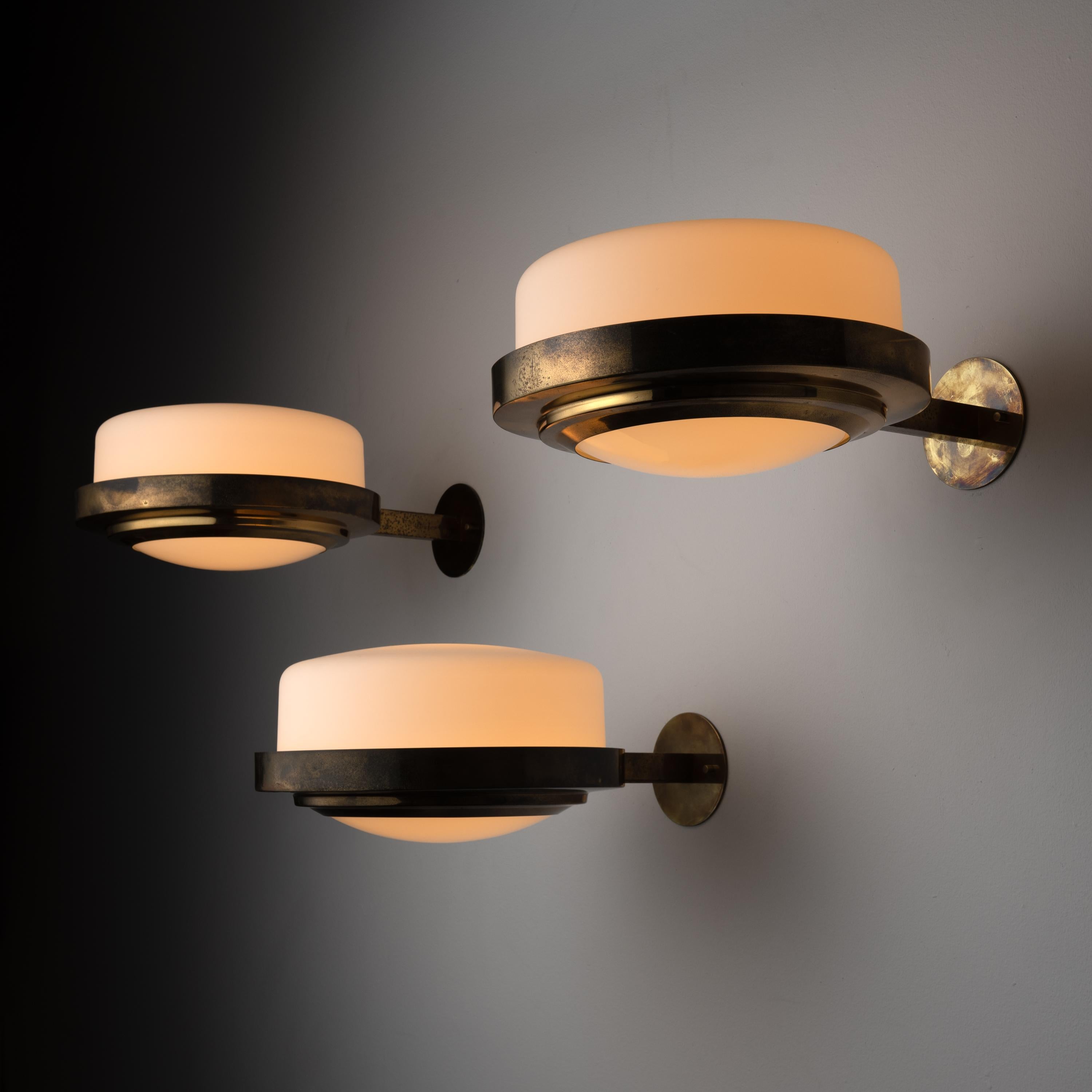 Rare sconces by Stilnovo. Designed and manufactured in Italy, circa 1960. These sconces contain a flush brass wall mount that is connected to a circular horizontal holder that carries a top frosted opaline glass shade, with a supporting opaline