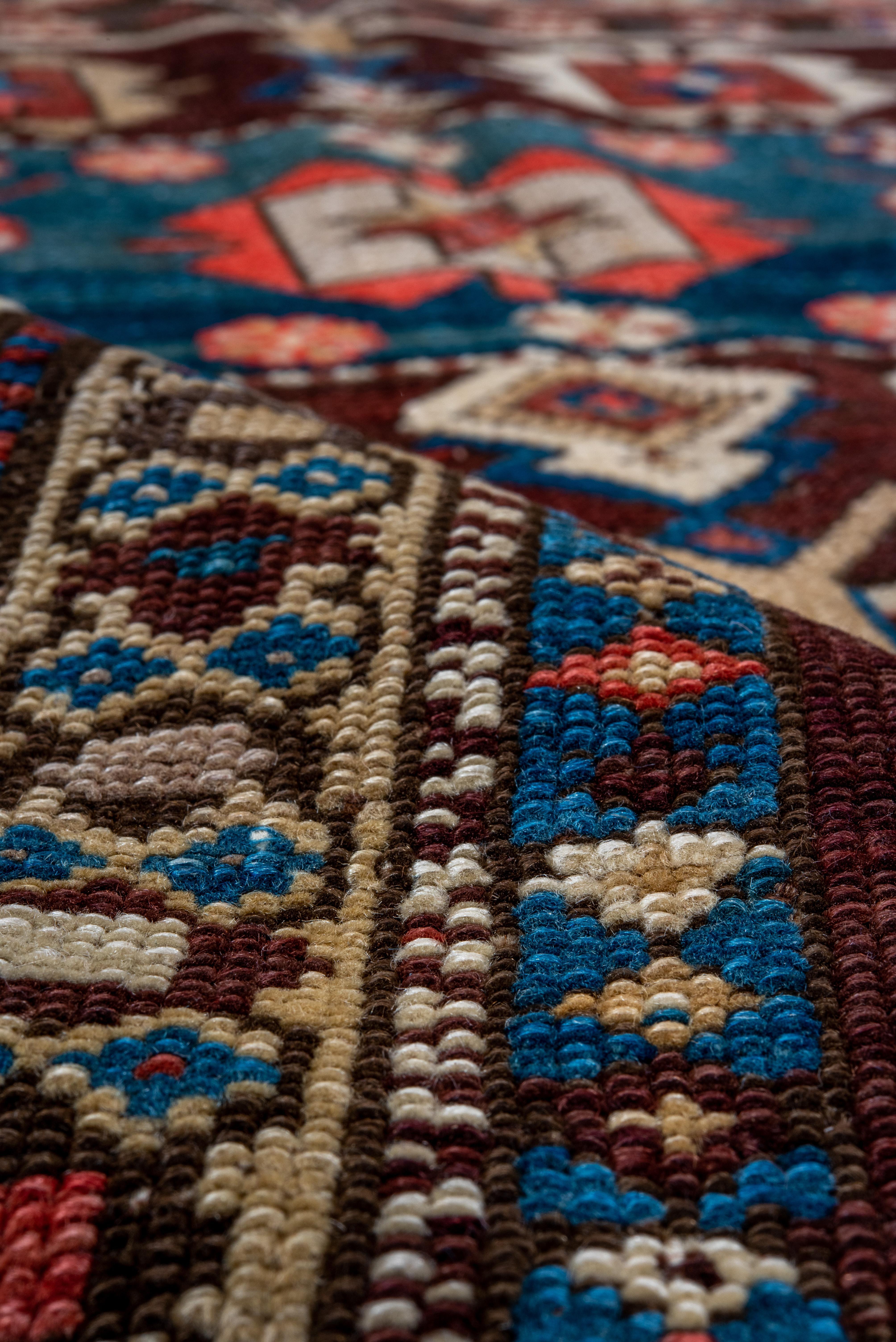 This relatively rare well-woven Eastern Caucasian carpet (as opposed to scatters) shows a saturated brick red field with three connected square octogramme panels in blue, cream, red and beige. The field shows large botehs toward one end, and small