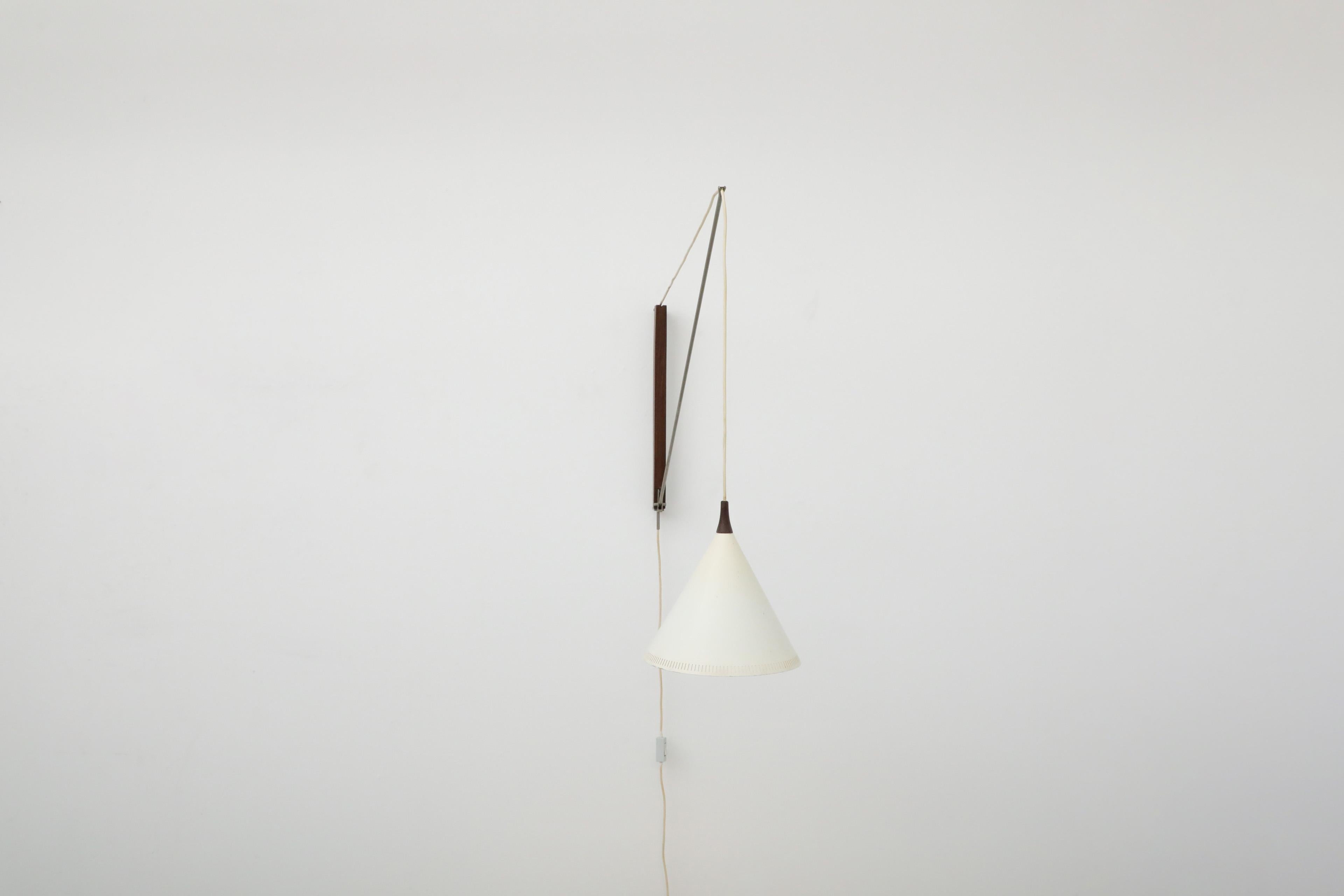 Beautiful Willem Hagoort wall sconce with white enameled metal cone shade on steel stem and teak wall mount and accent. This incredibly constructed light swivels and can be raised or lowered by adjusting its cord while providing an illuminating