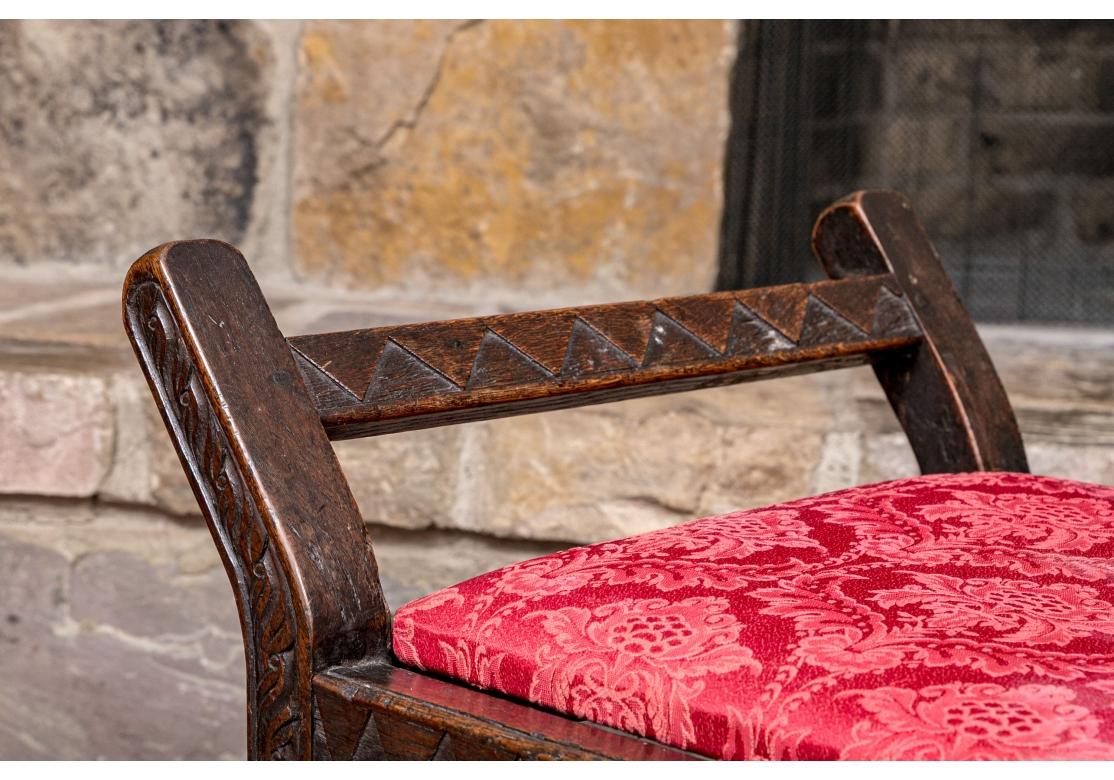 A rare early 18th century carved oak daybed with fine Primitive form. The frame with turned bobbin stretchers, geometric and stylized bird of prey carvings. The flat cushion upholstered in a deep rose foliate fabric. The frame with an overall