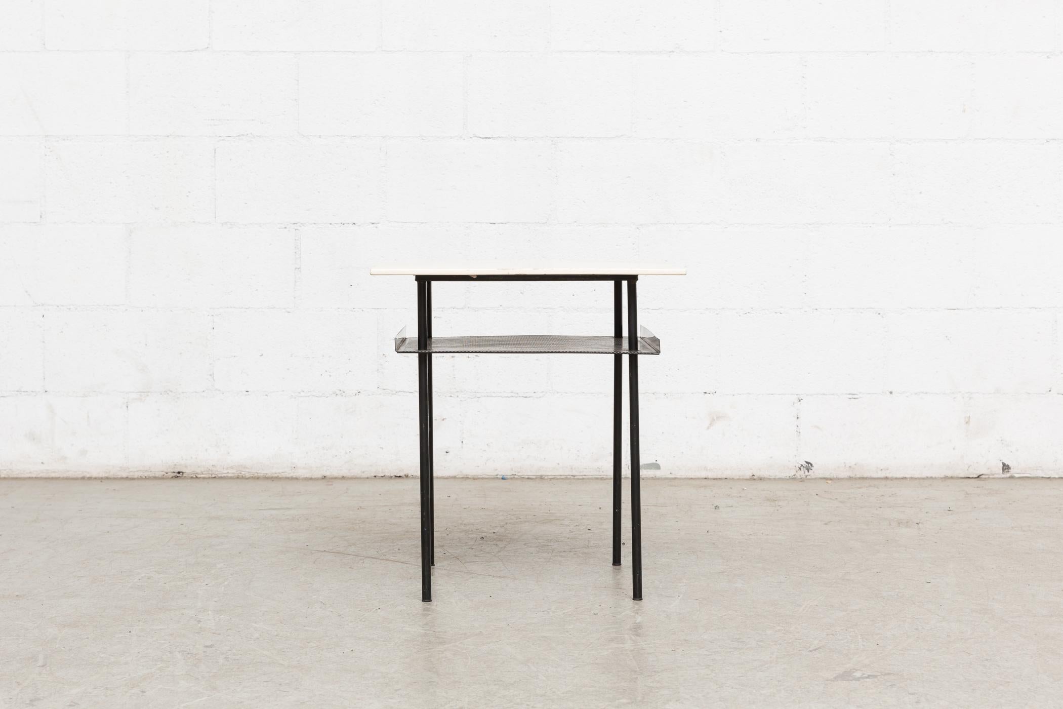 Smaller version of this side table in painted off-white plywood top with enameled black metal frame and perforated sheet metal lower shelf with bent edges. In original condition with visible wear to the top and frame.