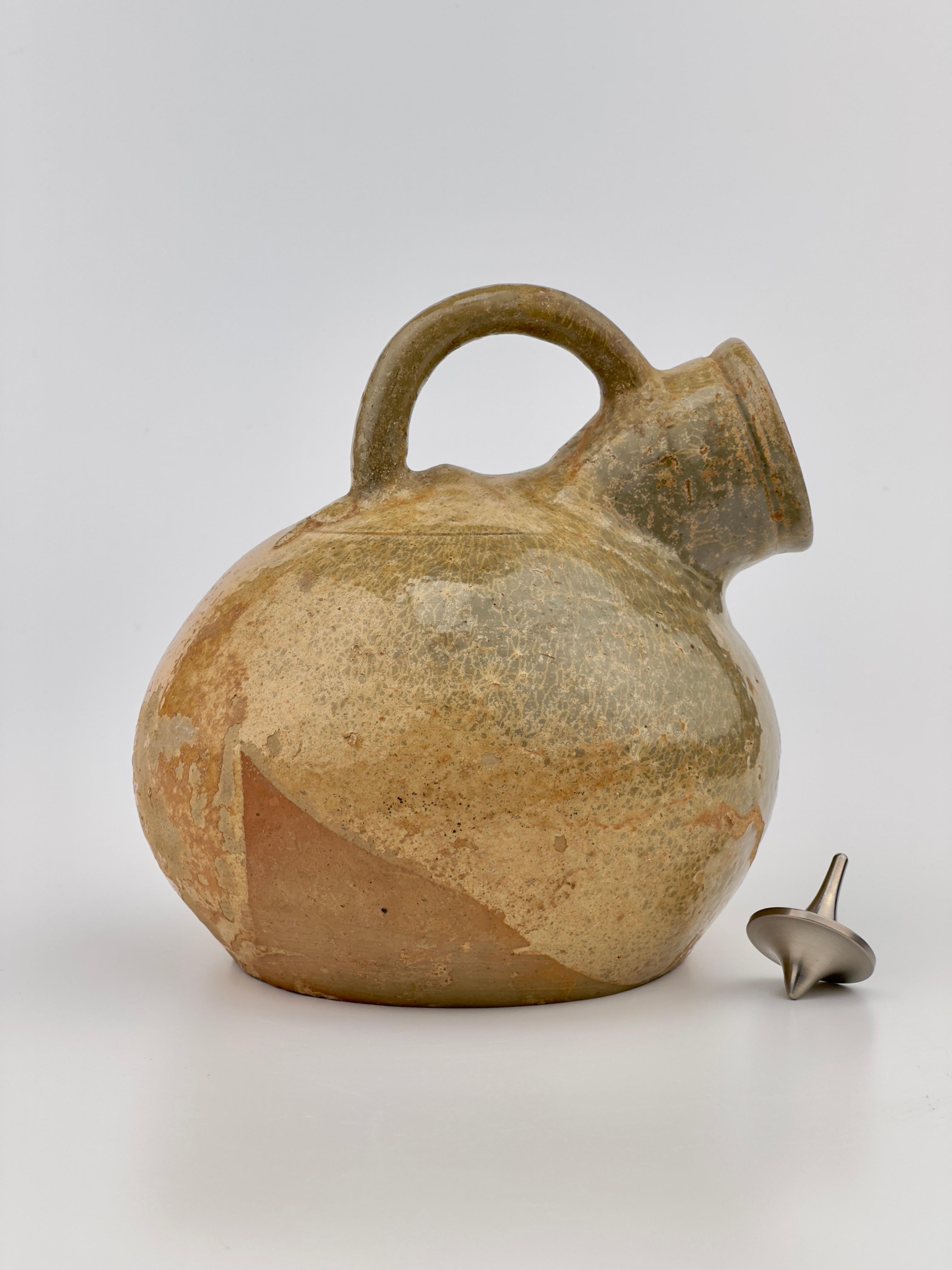 A Yue celadon vessel from the Jin Dynasty period, notable for its characteristic greenish-glazed pottery which was prominent during this time. The vessel features a globular body with a single looped handle that arches gracefully from the shoulder