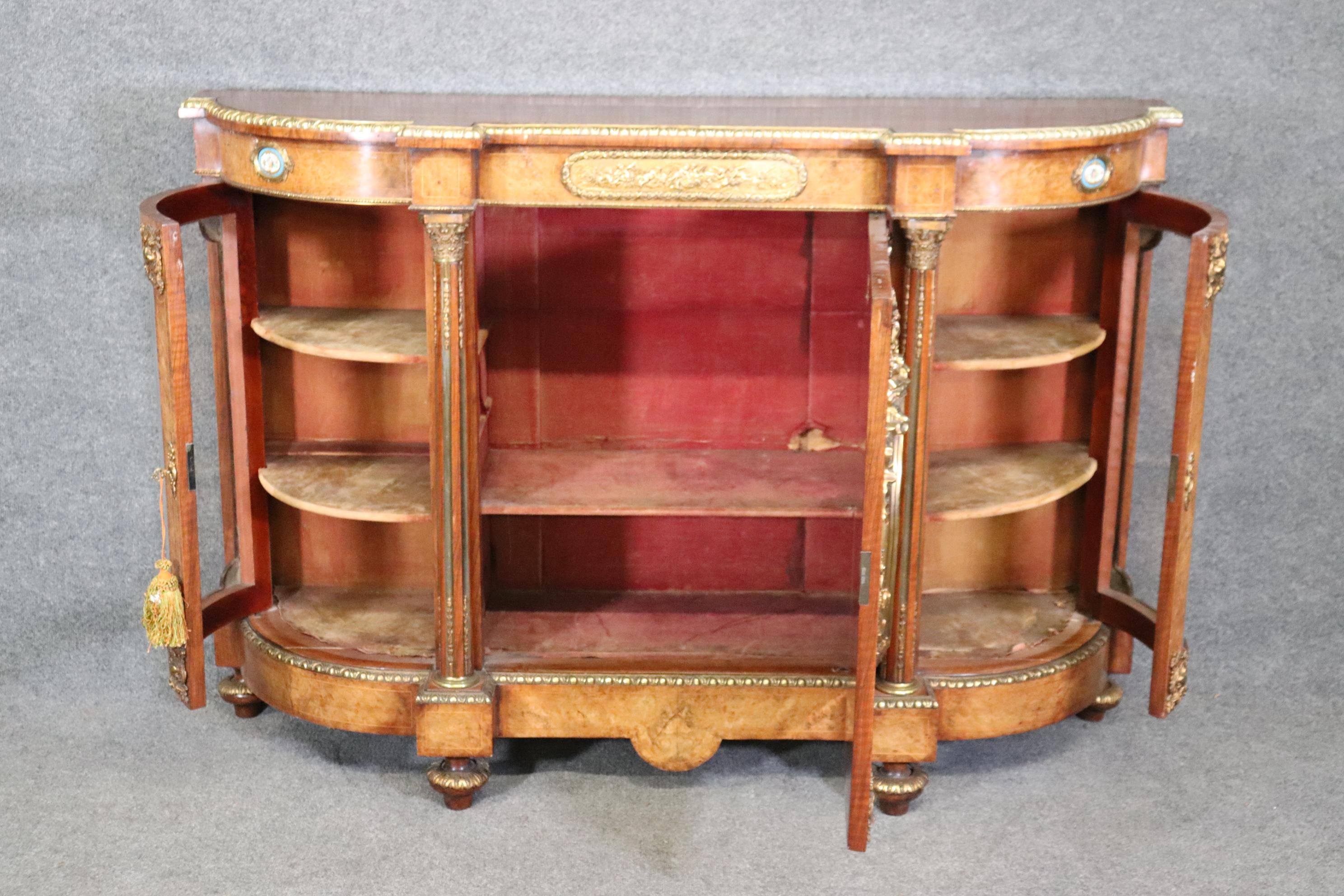 This is a remarkable Druce & Company burled walnut sideboard with some of the finest bronze mounts, porcelain plaques and it's original red velvet interior with bowed glass ends and a glass vitrine door in the center. The sideboard was designed to