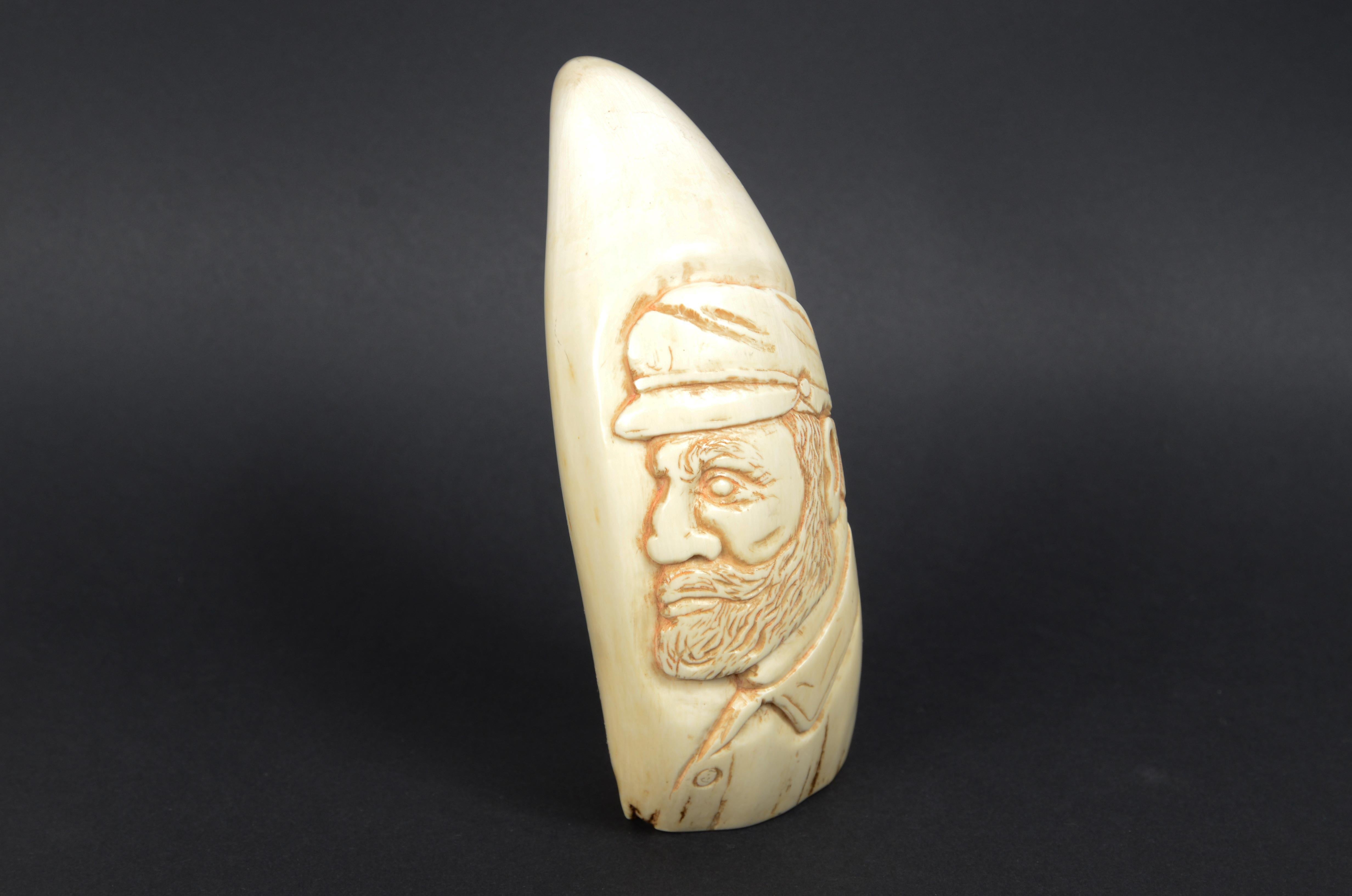 Rare scrimshaw of a large whale tooth depicted vertically in bas-relief  the profile of a bearded whaler with hat on his head, height 16 cm. Datable to around the mid-19th century. On the back  the following engraved inscription: Here's death to the