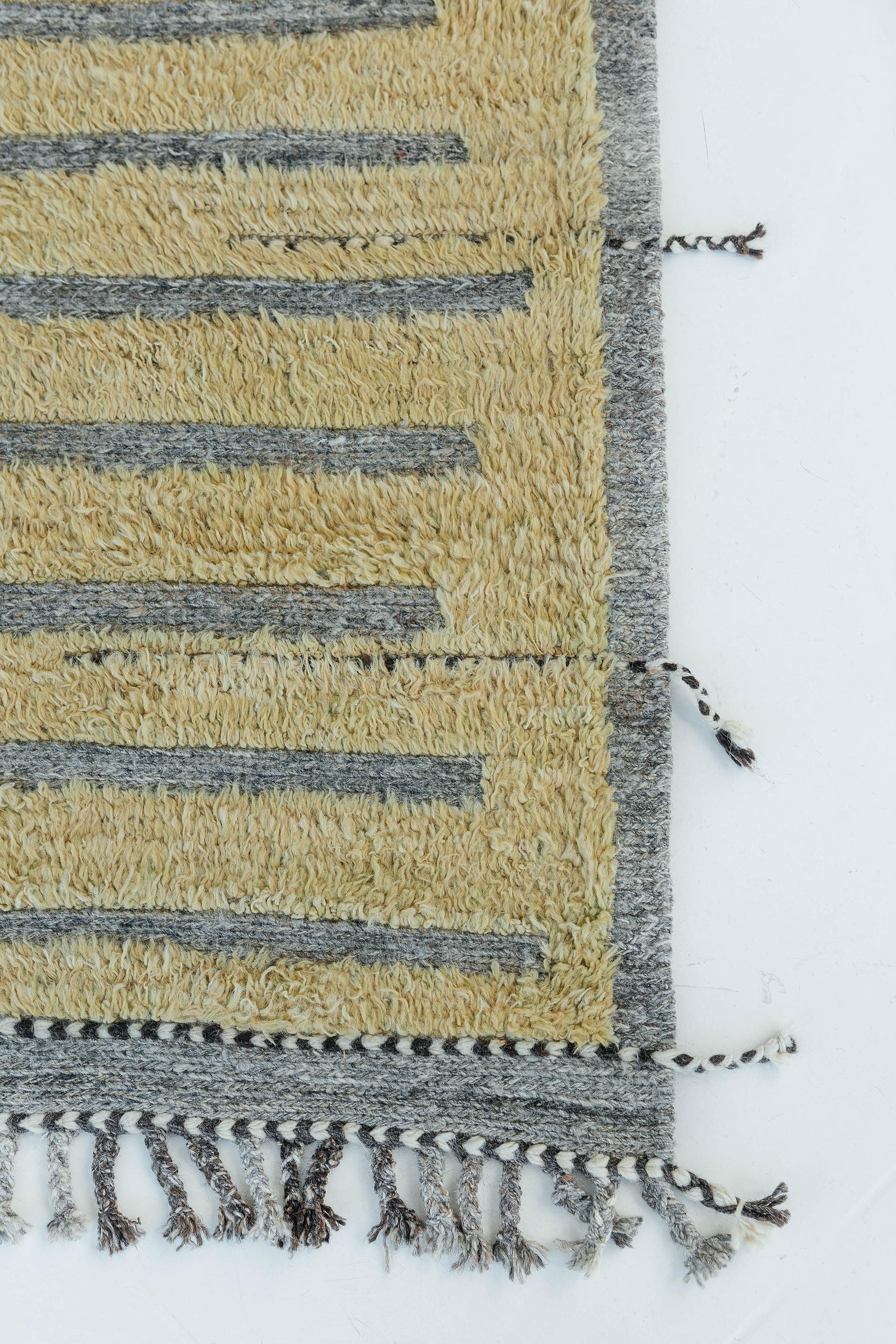 Handwoven of wool, Rashabar uses linework and color to create definition and movement. Embossed detailing of charcoal and taupe-grey moves across the rug with a yellow shag surface. Natural flat weave runs around the border with tasseled