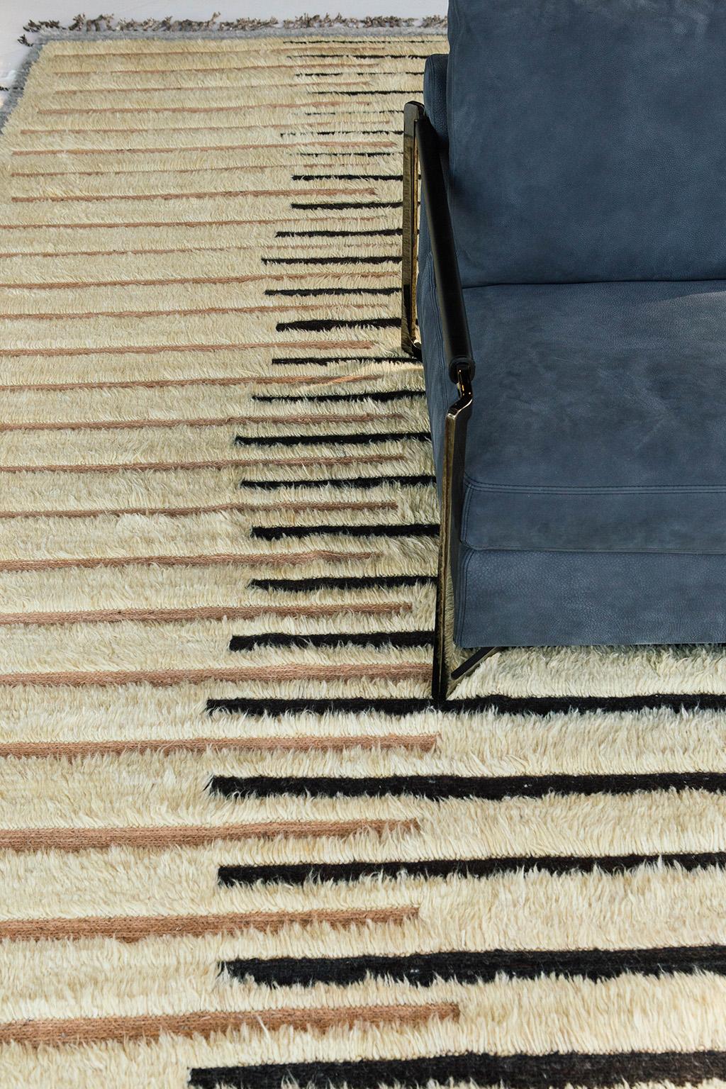 Handwoven of wool, Rashabar uses line work and color to create definition and movement. Embossed detailing of natural black, light brown and taupish grey move across the rug with a yellow shag surface. Natural flat weave runs around the border with
