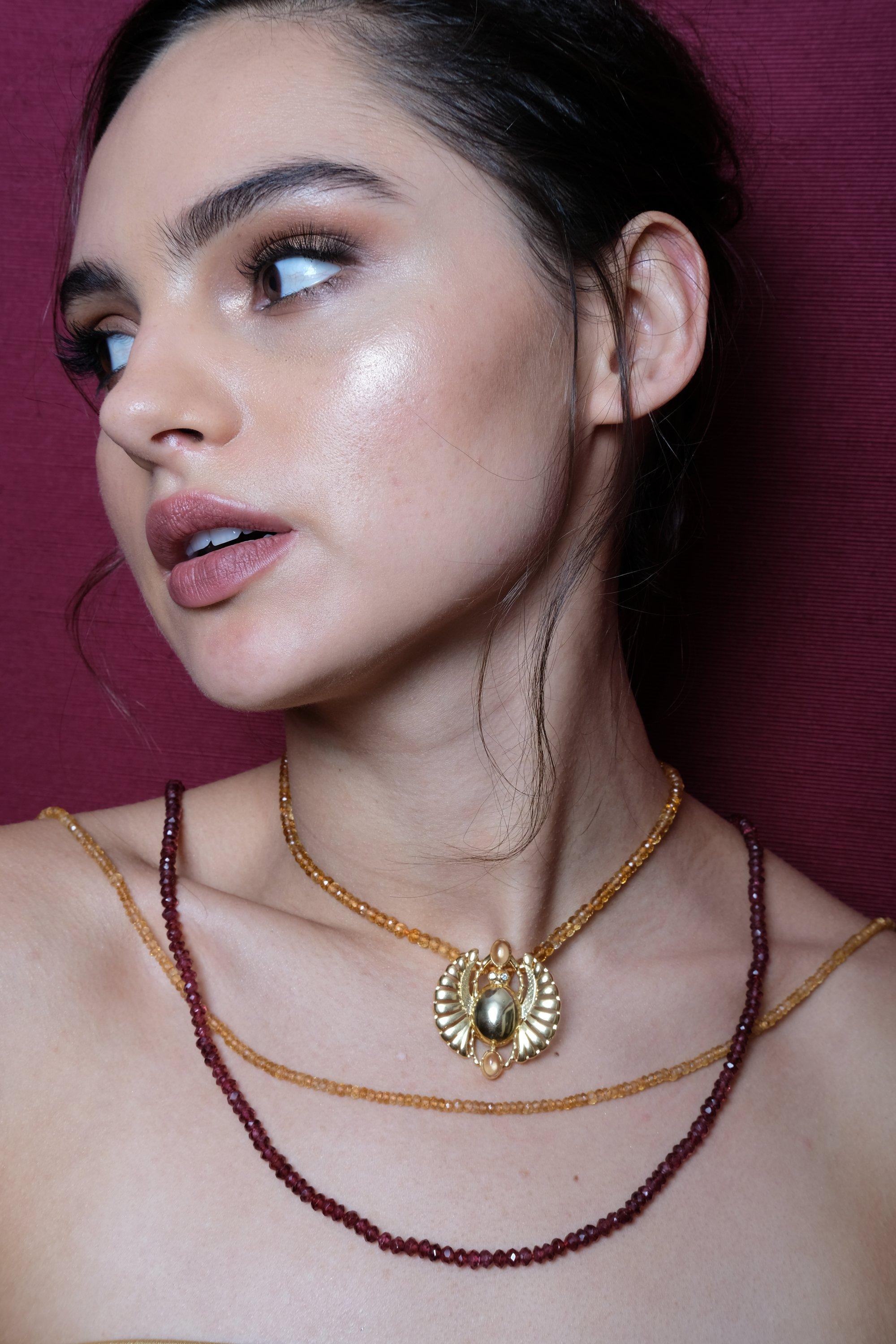 This necklace in precious metals and semiprecious stones is a timeless statement with the open winged scarab pendant. The pendant comes in yellow gold vermeil and Sterling silver. Its all-around stones feature vivid color colors with cabernet red