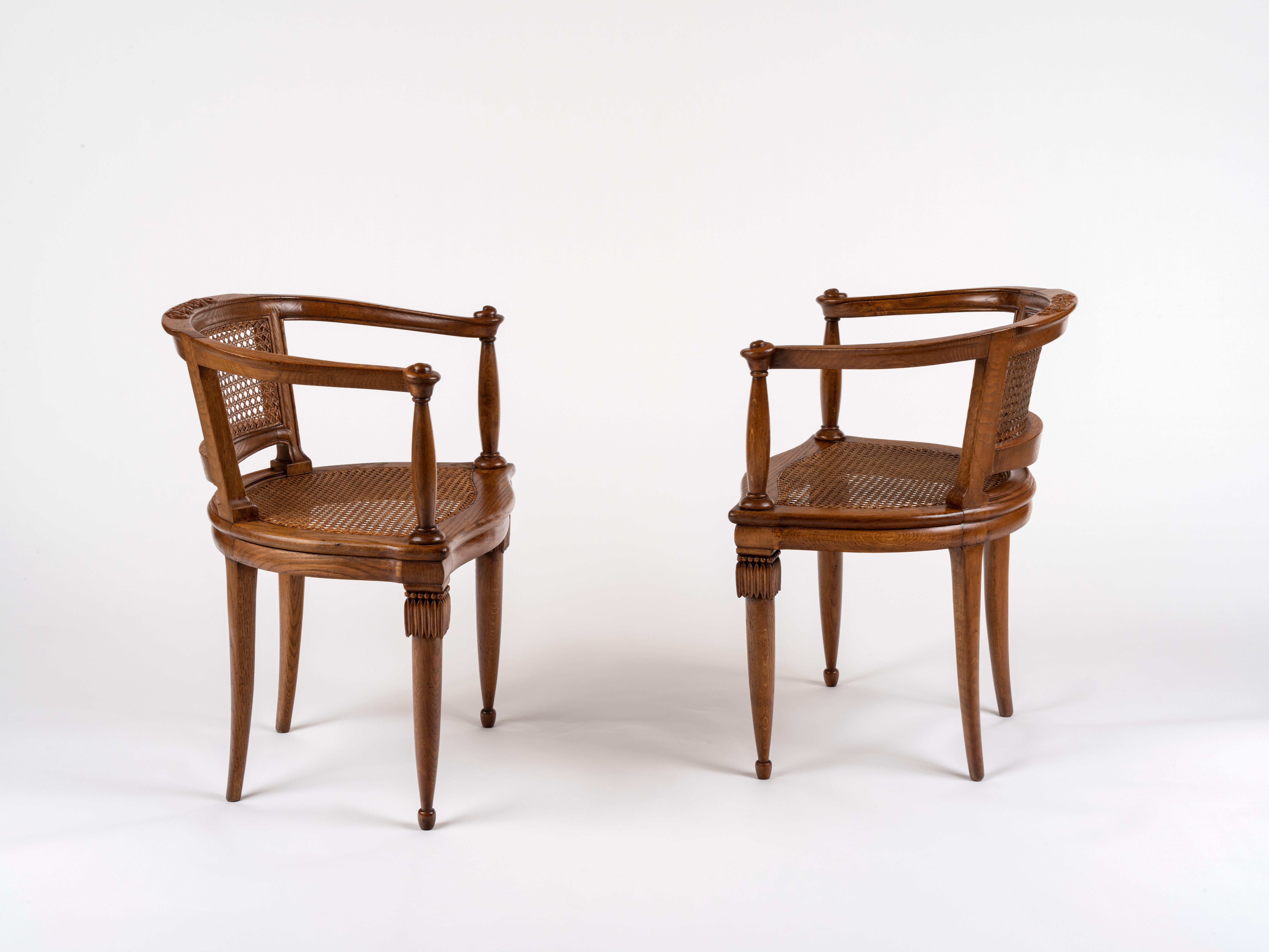 A pair of oak armchairs by Armand-Albert Rateau. Feautring curled arm supports, wide caned seats and  caned concave backs, both chairs stand on two carved and tapered front legs, sculpted each at the top with stylized bunches of grapes. The back